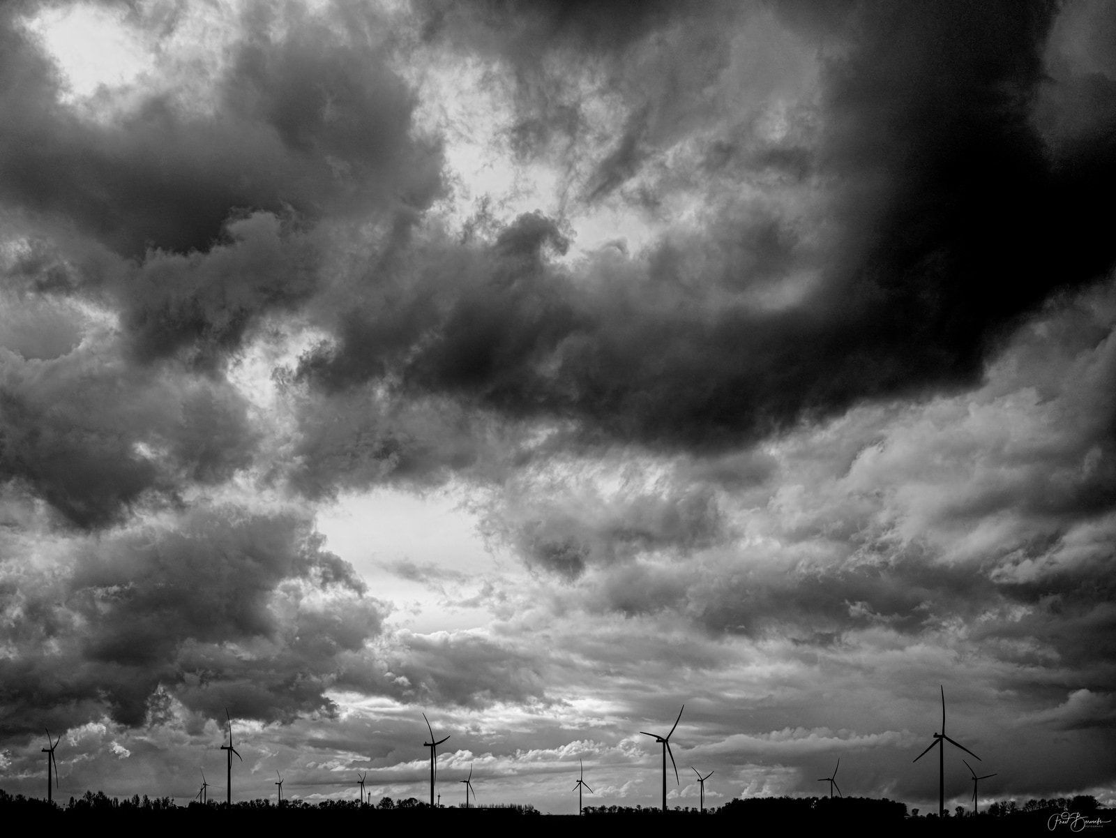 Wind turbines stand silhouetted against a dramatic, brooding sky filled with dense, dark clouds.