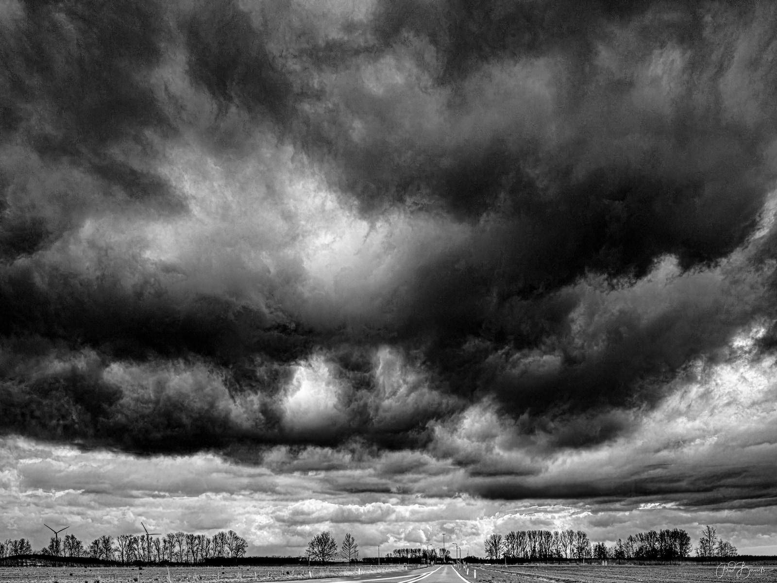 A dramatic sky with dark, heavy clouds dominates the scene, with a bright sun breaking through the clouds and a flat, open landscape below.