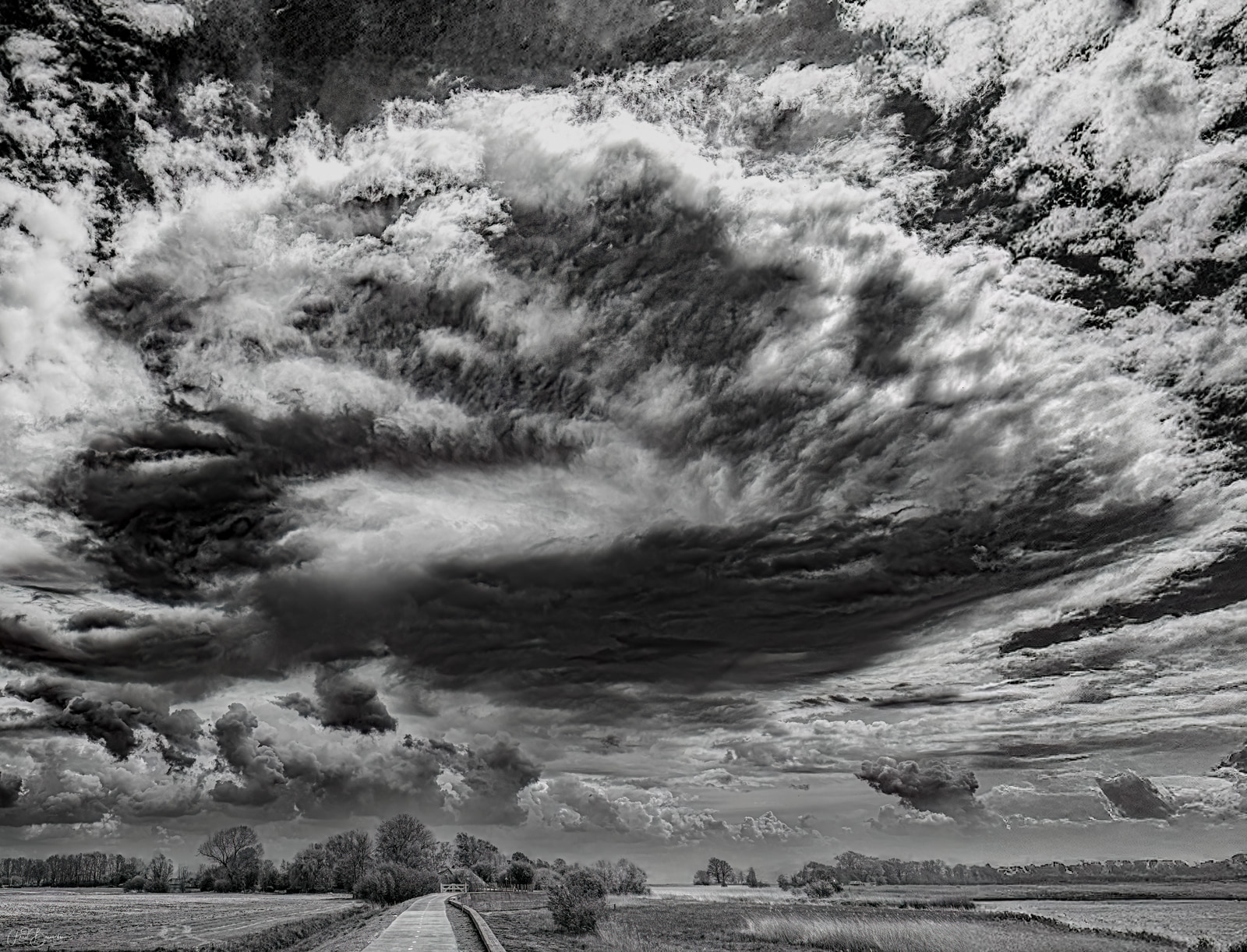 A wide, open field stretches beneath a dramatic, brooding sky filled with dense, layered clouds.