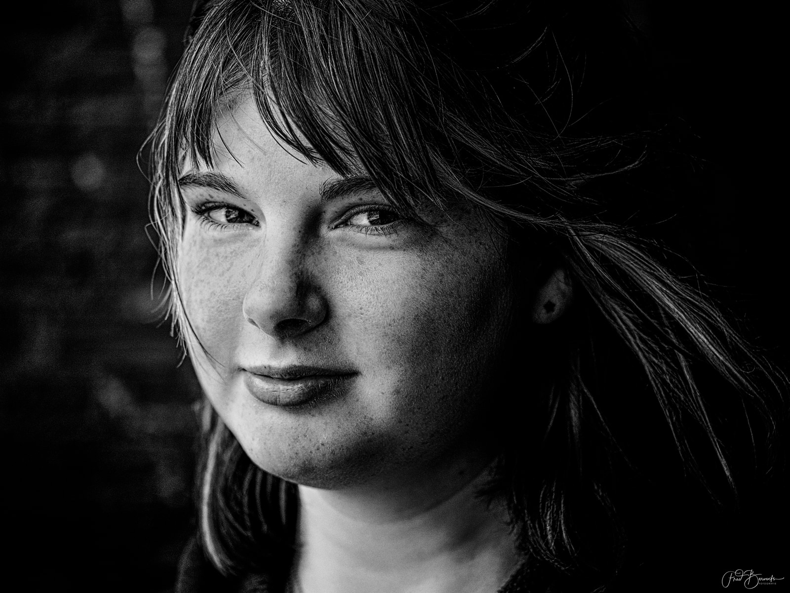 A close-up portrait of a person with long hair, captured in black and white with dramatic lighting.
