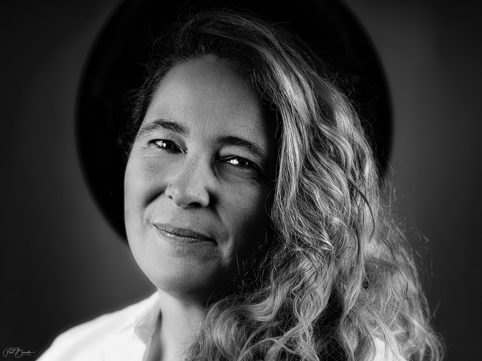 A person with long, wavy hair gazes directly at the camera against a dark background.