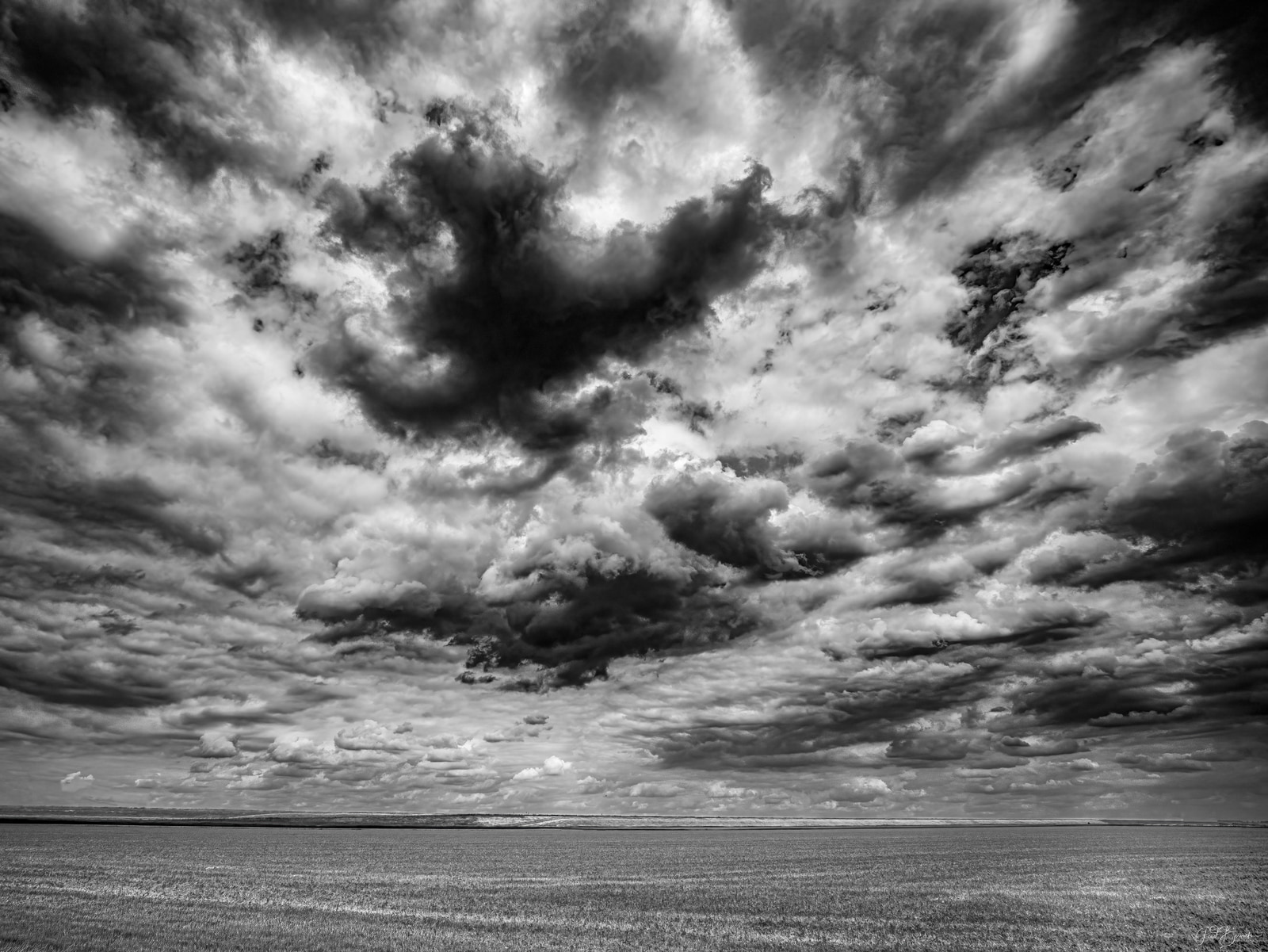 A vast field stretches beneath a dramatic sky filled with dense, billowing clouds.