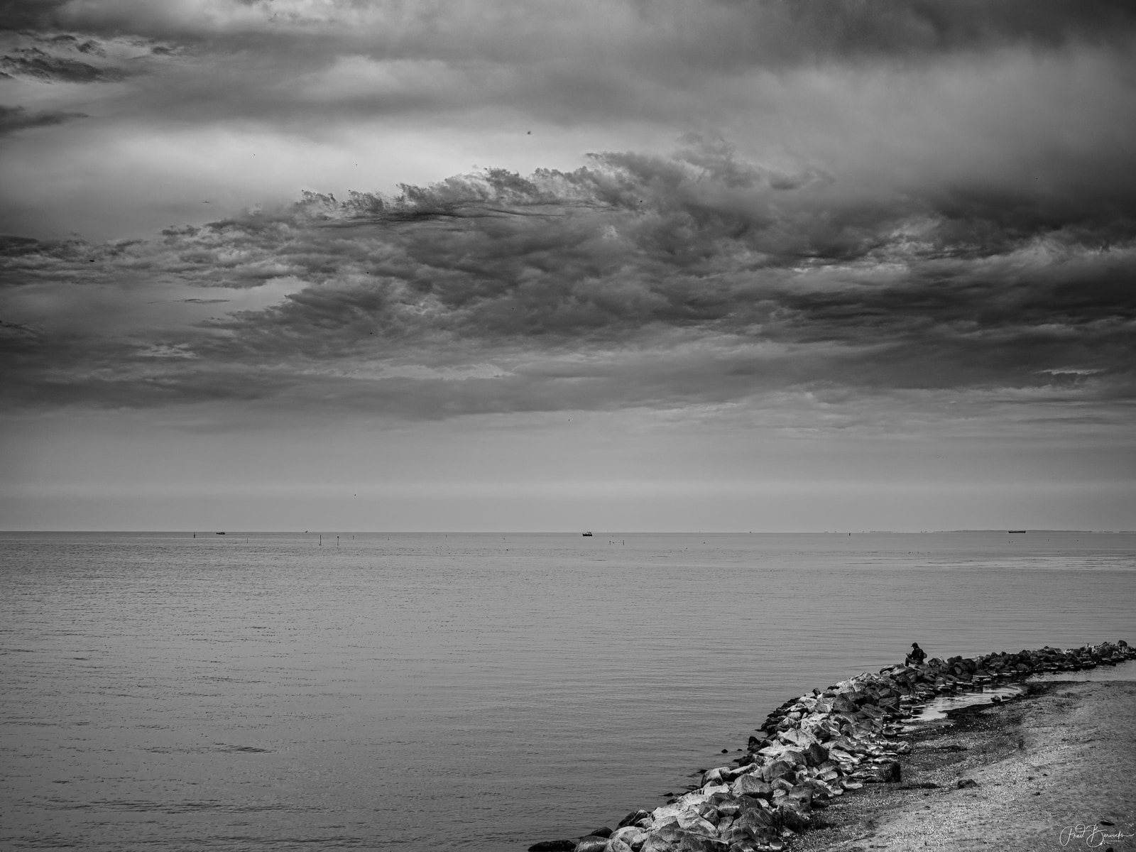 A vast sea stretches under a dramatic, brooding sky, with a rocky outcrop visible along the shoreline.