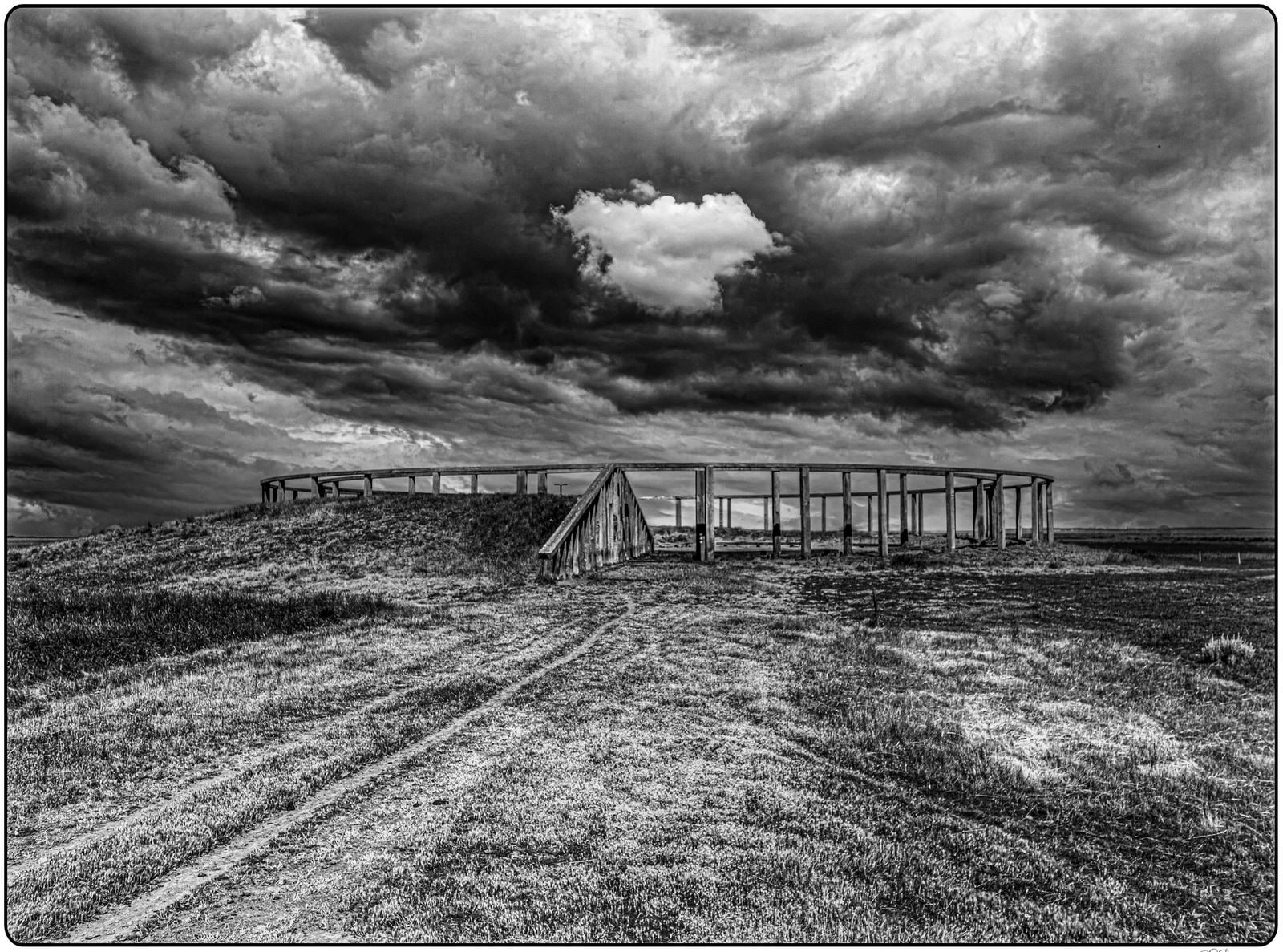 A long walkway extends across a grassy field under a dramatic, overcast sky.