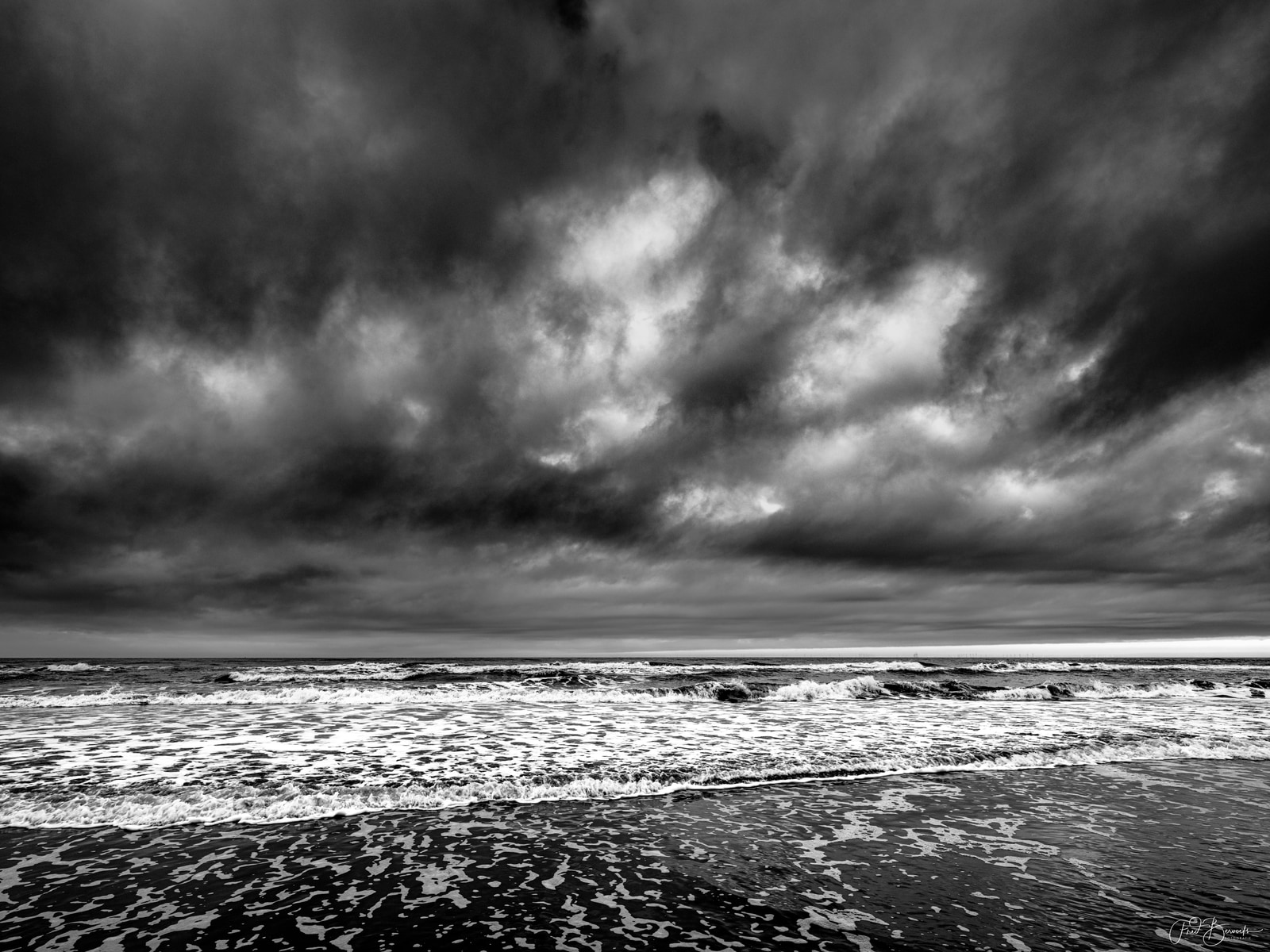 A dramatic seascape shows turbulent waves crashing against a beach under a brooding, overcast sky.