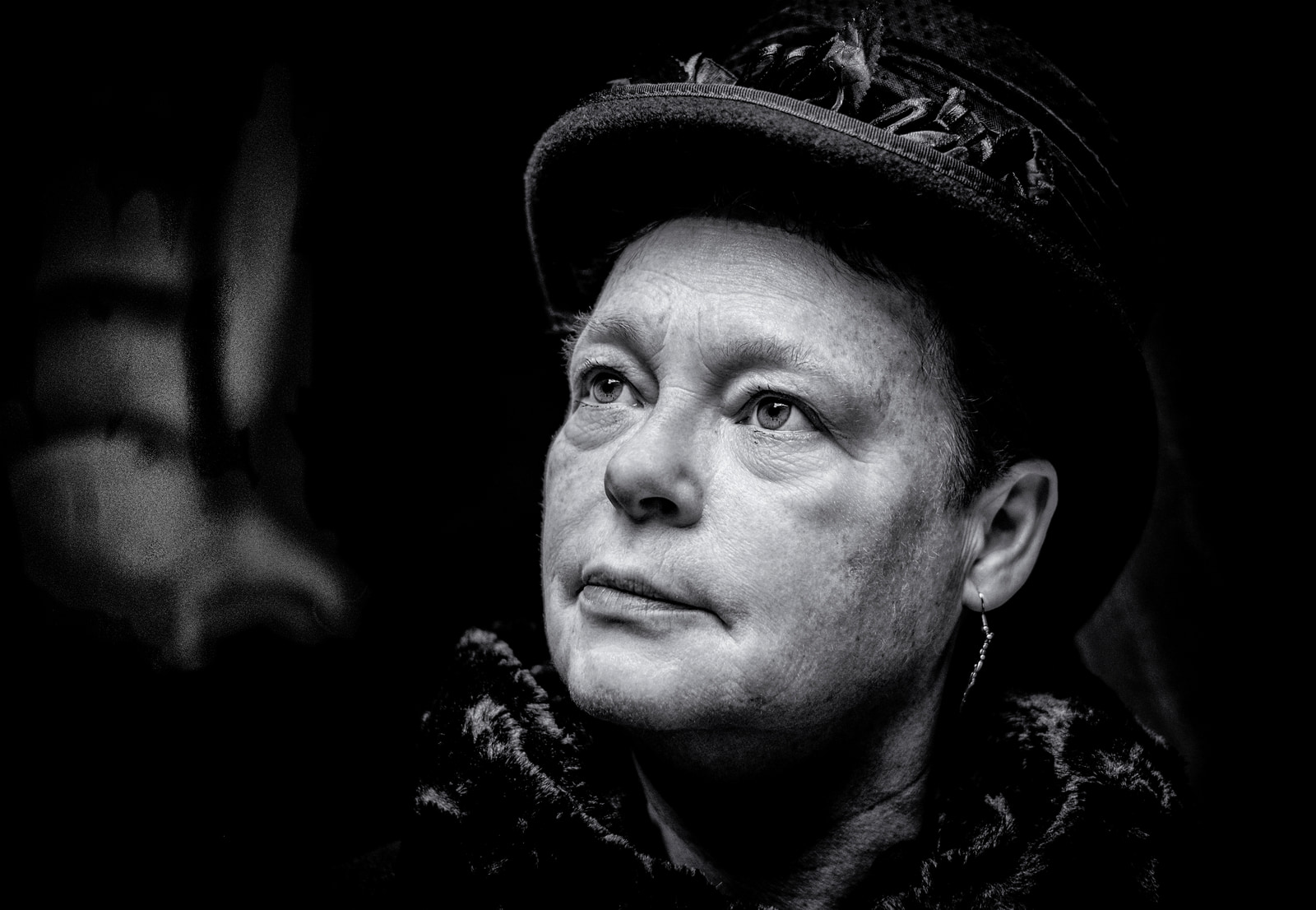 A person wearing a hat and a dark scarf looks to the side against a dark background.