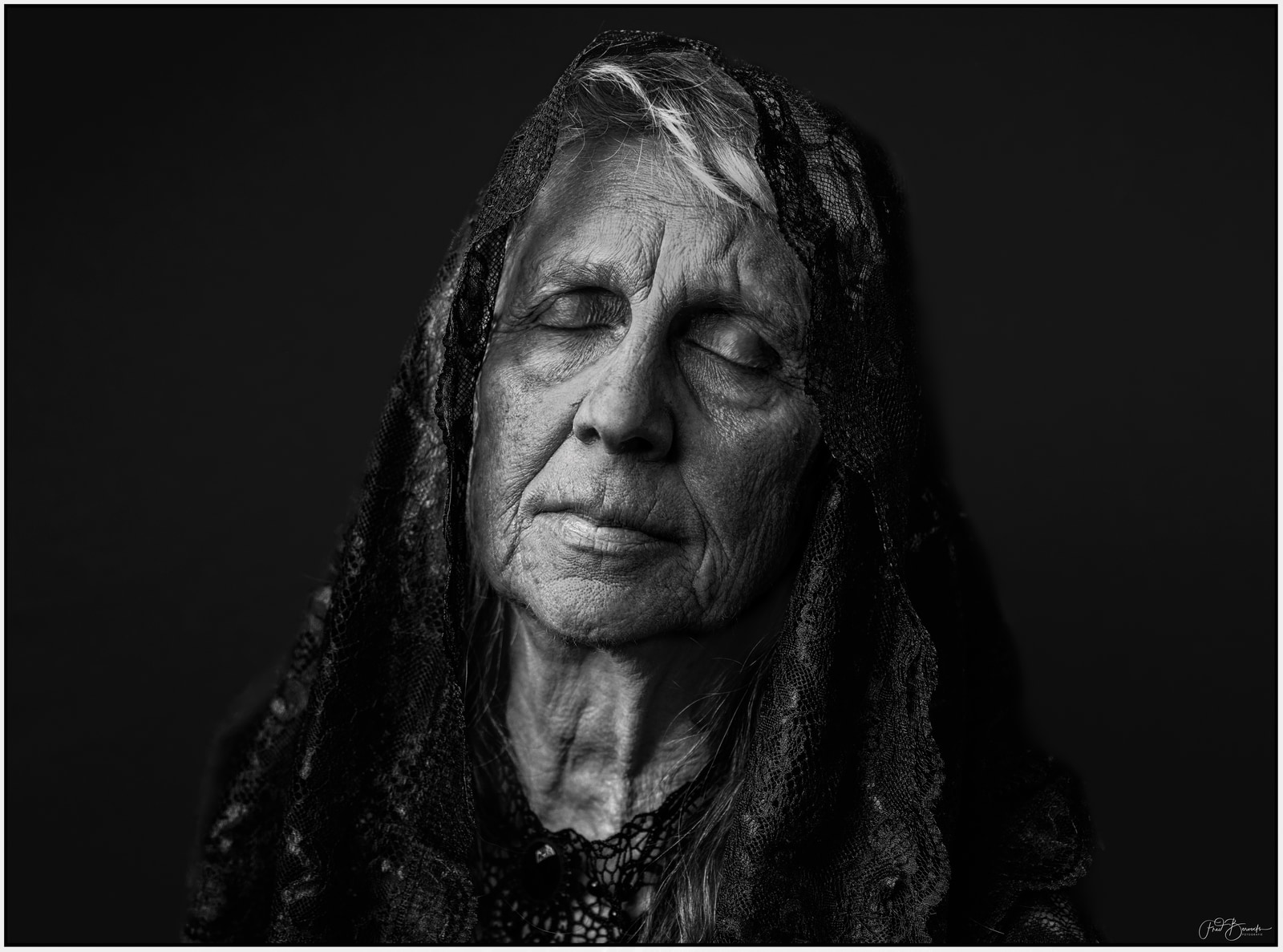 An elderly person with closed eyes and a textured head covering.