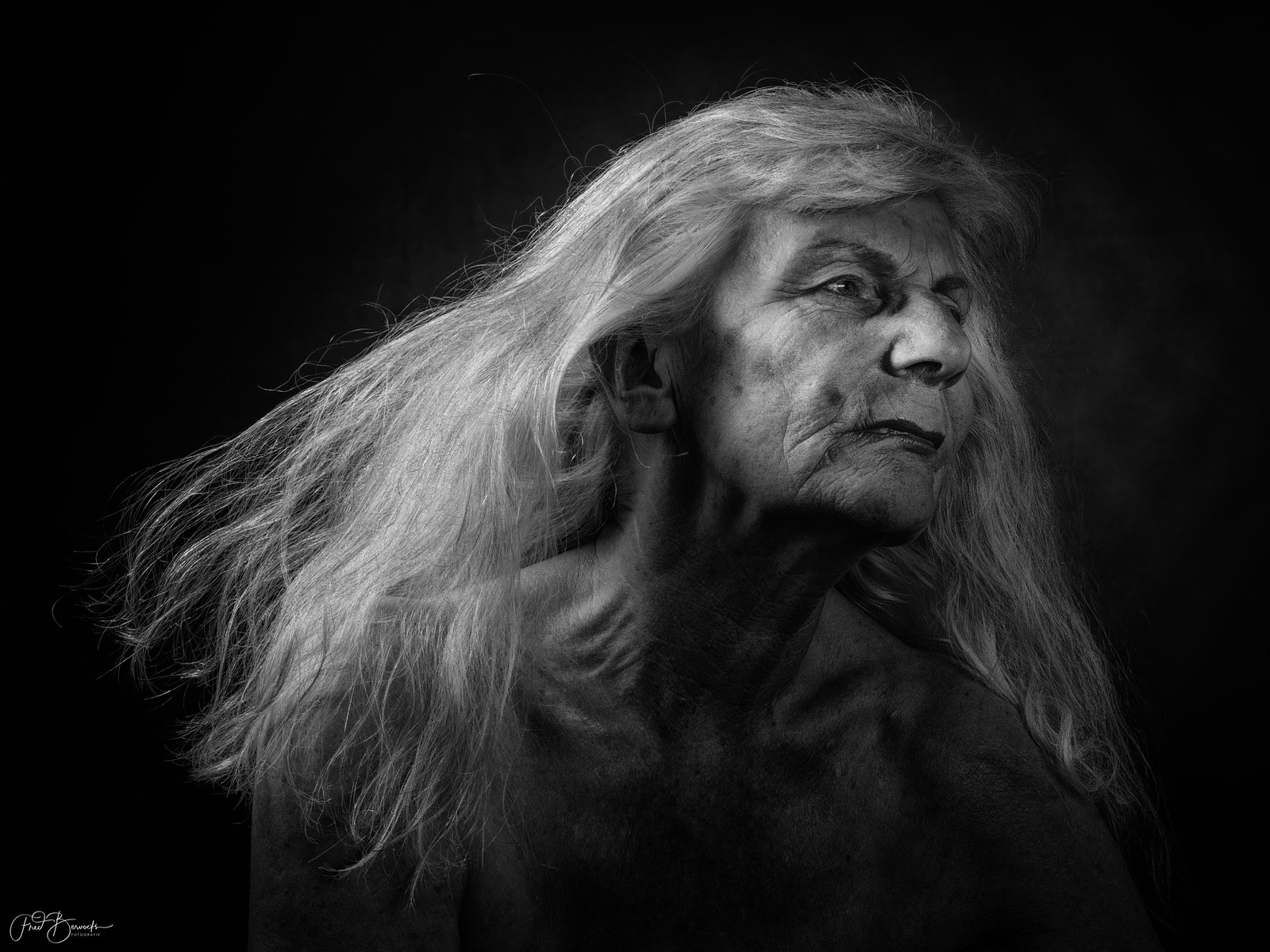 A person with long hair gazes to the side against a dark background.