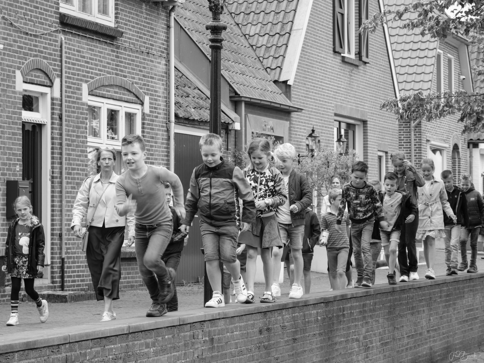 Children and adults walk together along a brick canal-side path in a historic town.