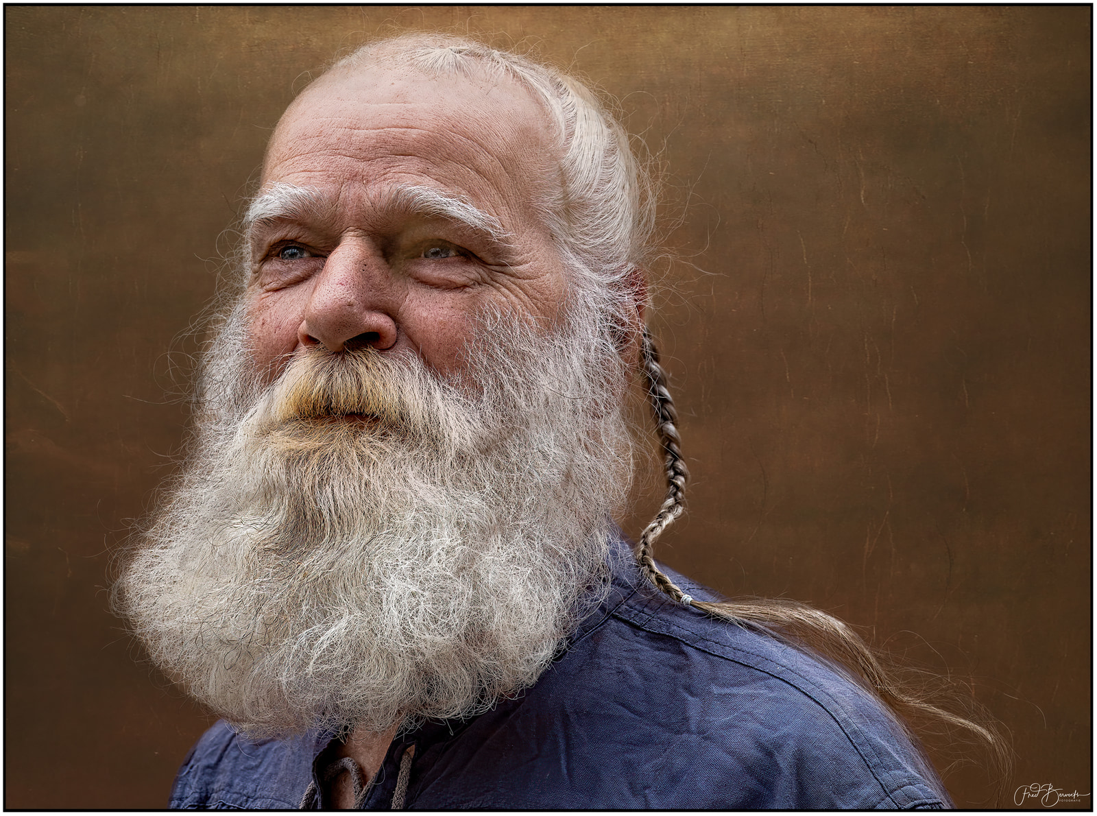 An older man with a long white beard and braided hair looks directly at the camera.