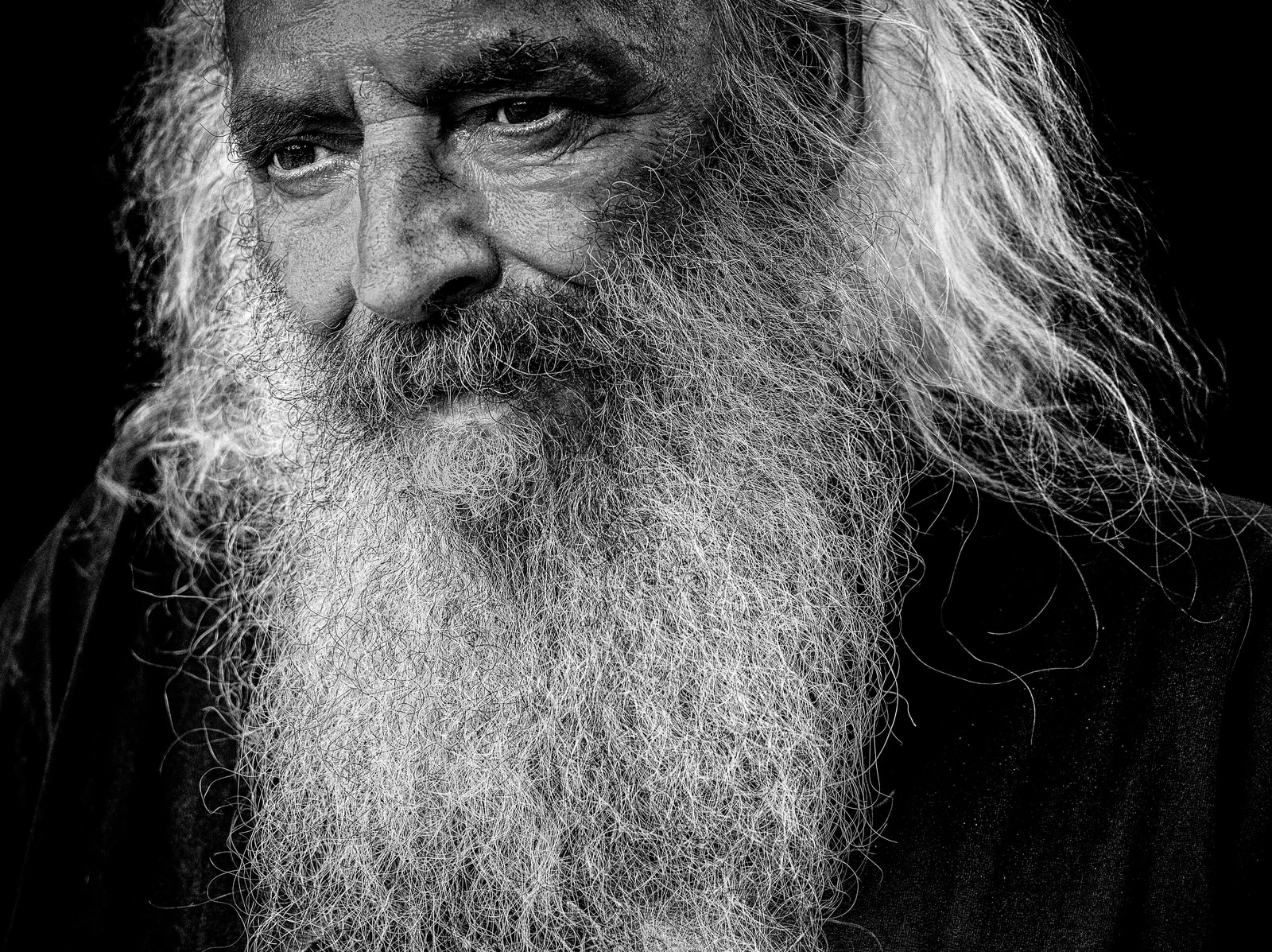 An elderly man with long white hair and a full beard gazes directly at the camera.