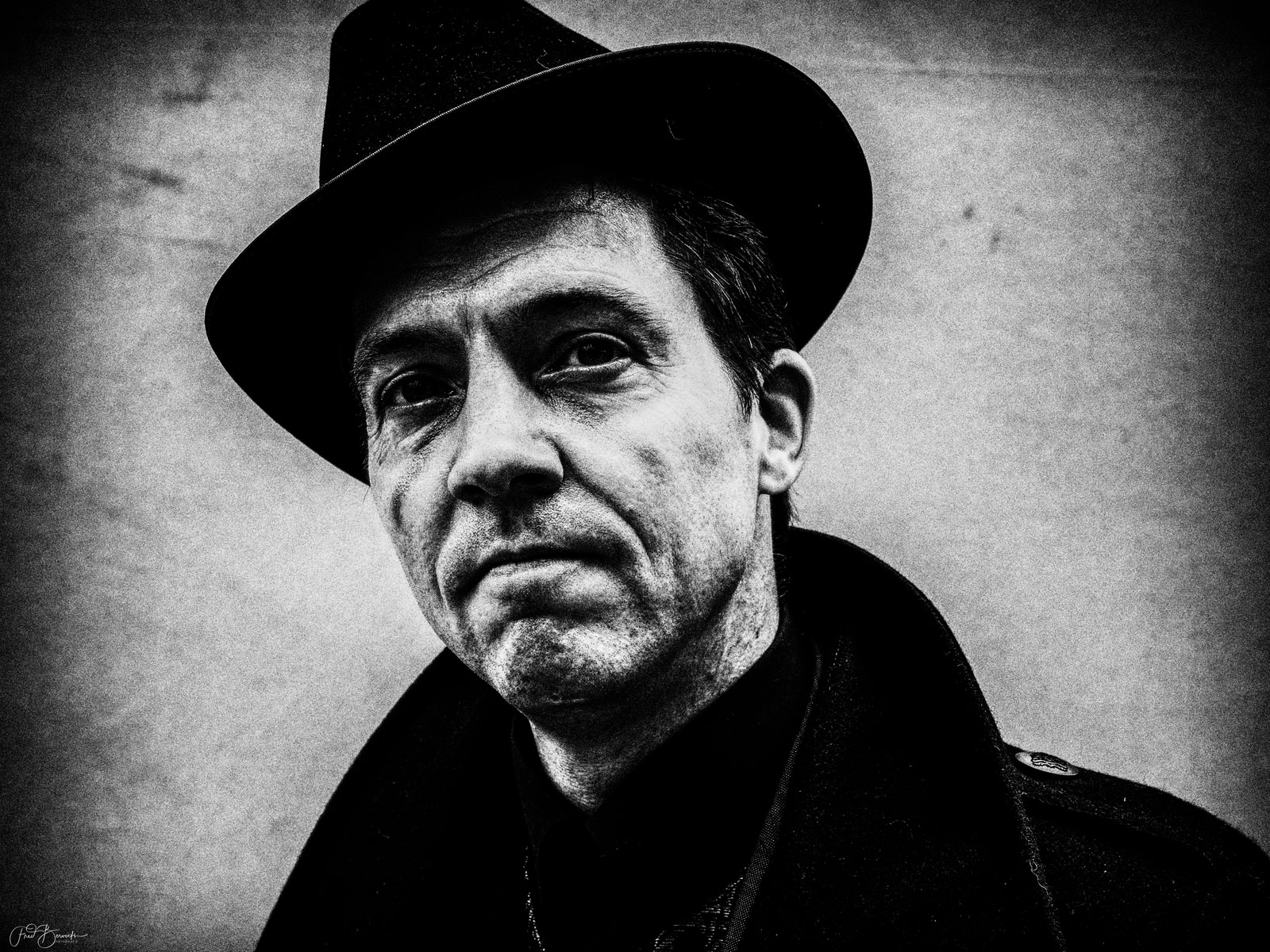 A man in a hat poses for a portrait against a dark background.
