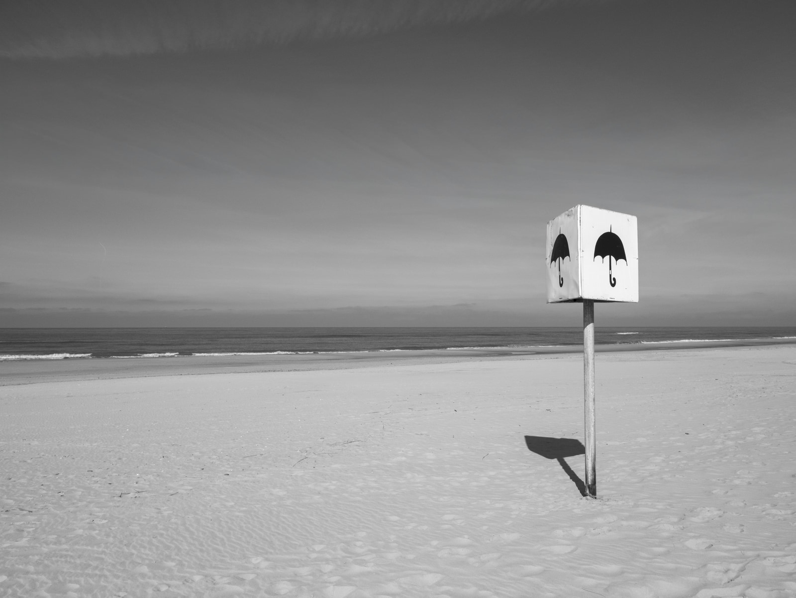 A white umbrella-shaped sign stands on a sandy beach under a cloudy sky.