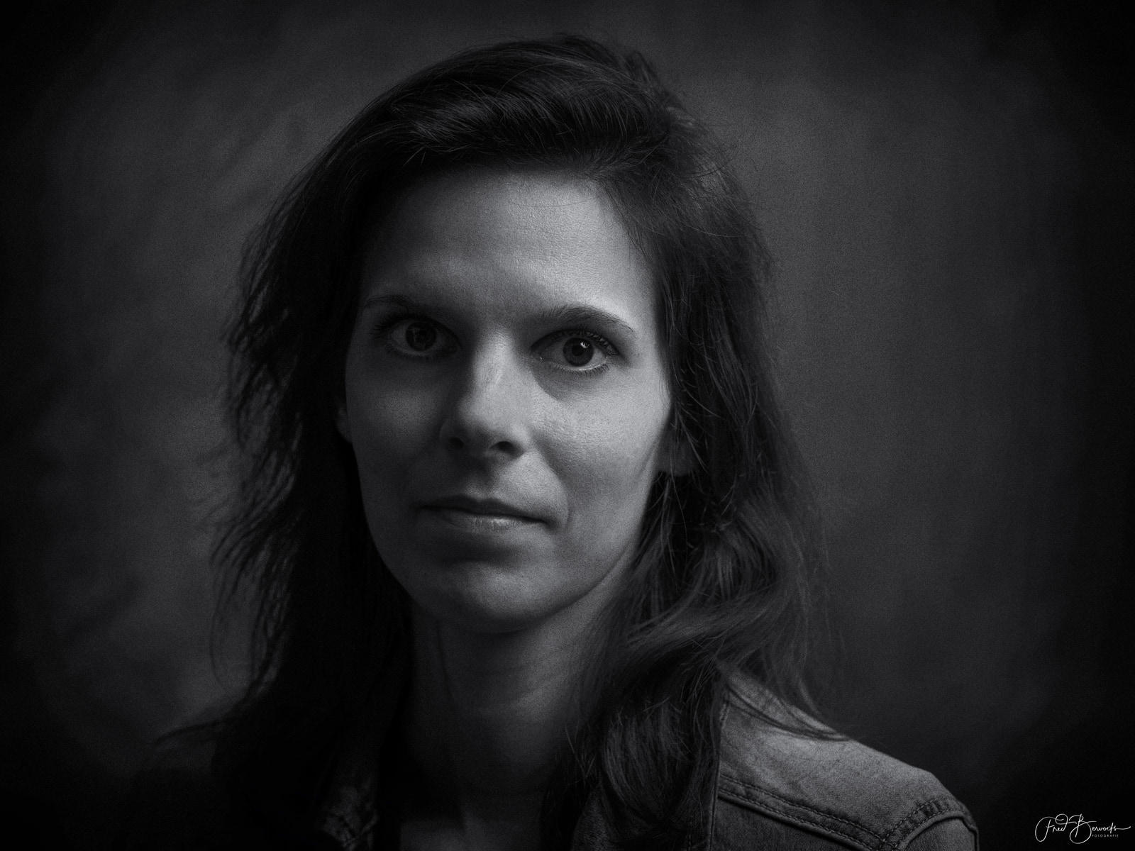 A person with long hair is shown in a close-up portrait against a dark background.