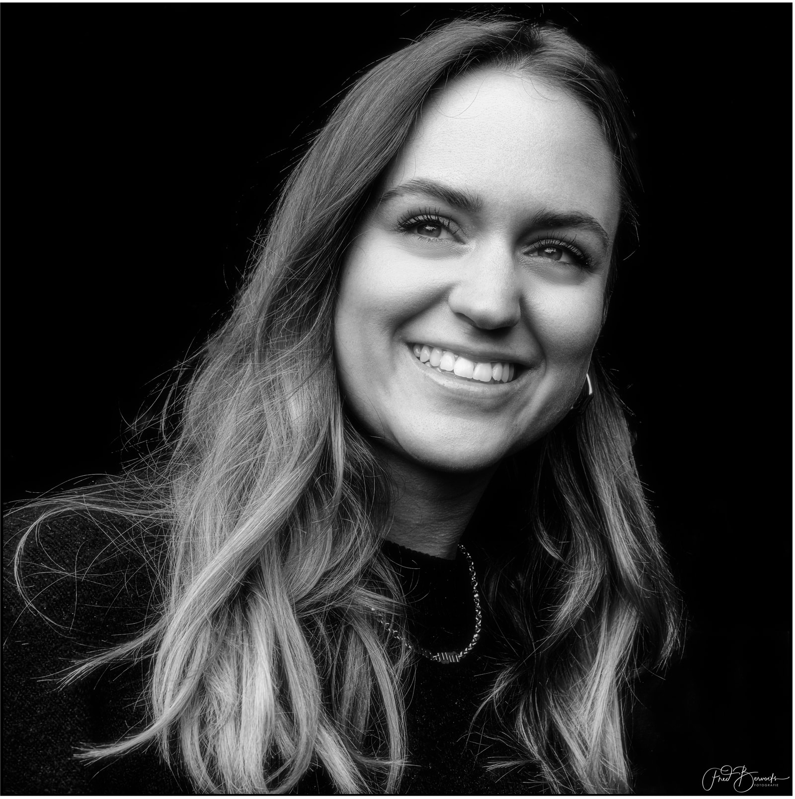 A woman with long hair smiles warmly against a dark background.