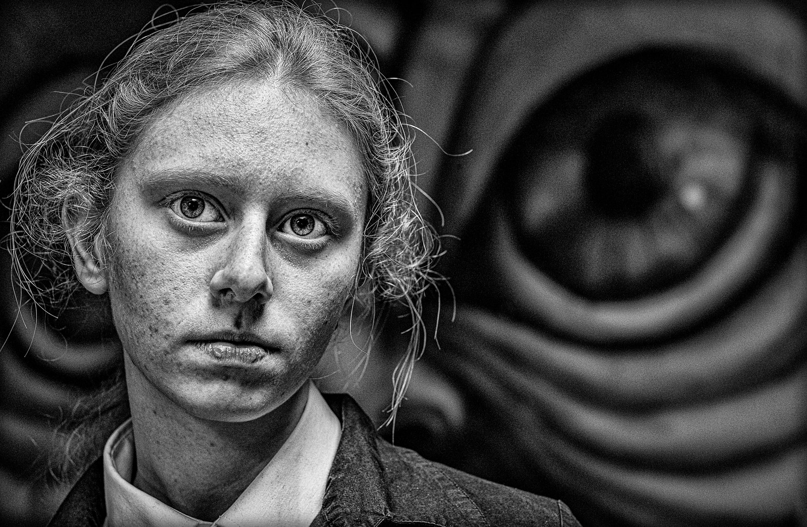 A person with disheveled hair looks directly at the camera with a serious expression.