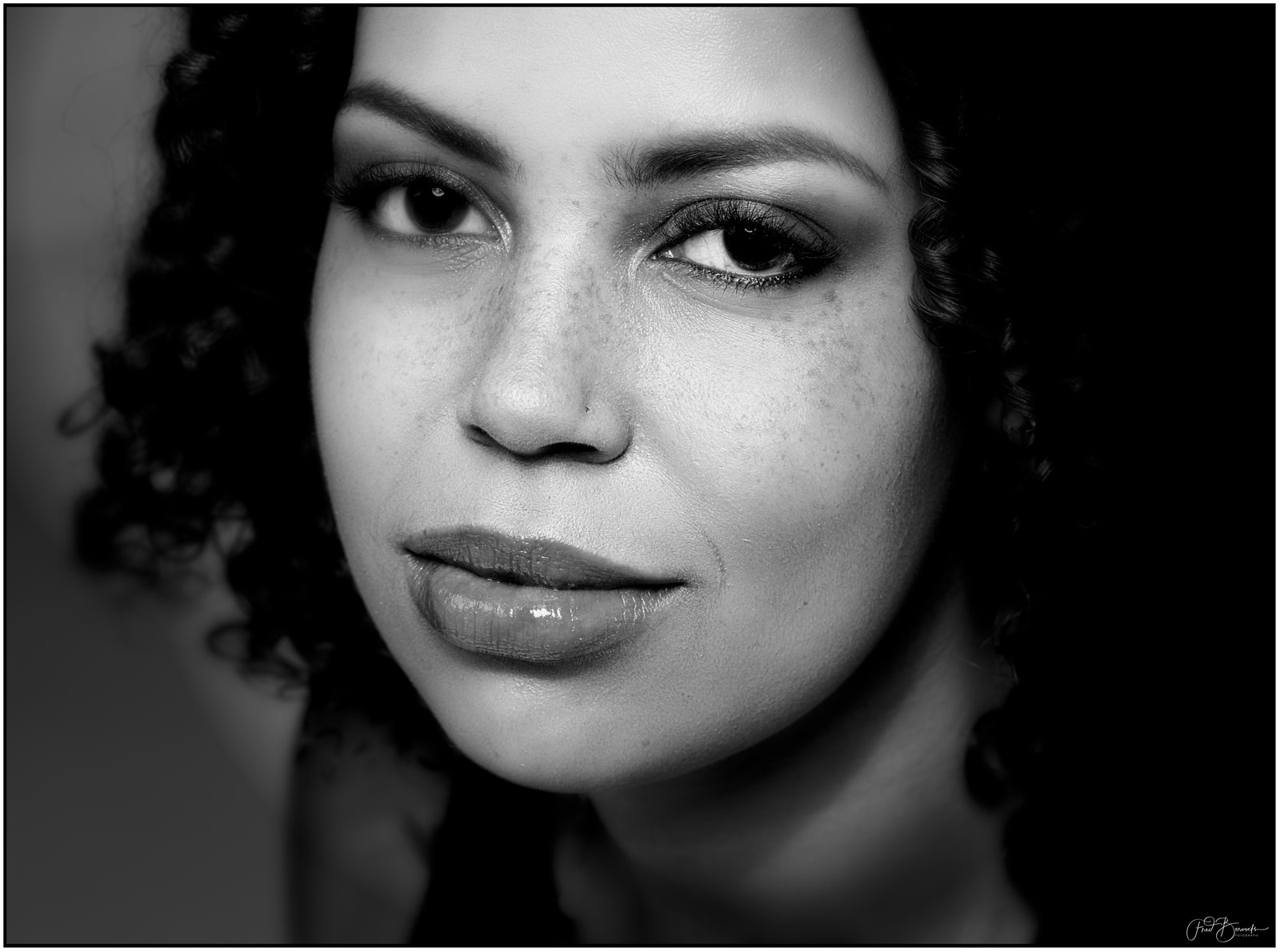 A close-up portrait of a person with curly hair, focusing on the eyes and mouth against a dark background.