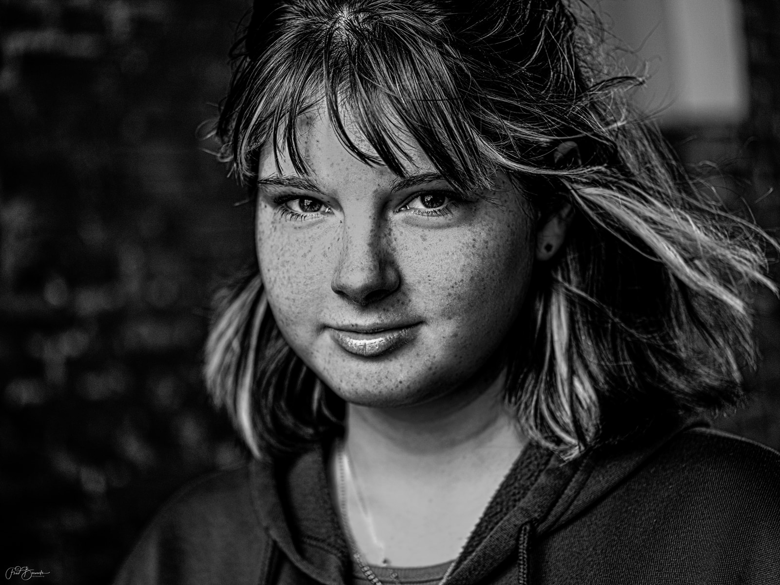 A young person with light-colored hair and freckles smiles gently, captured in a soft, monochromatic portrait.