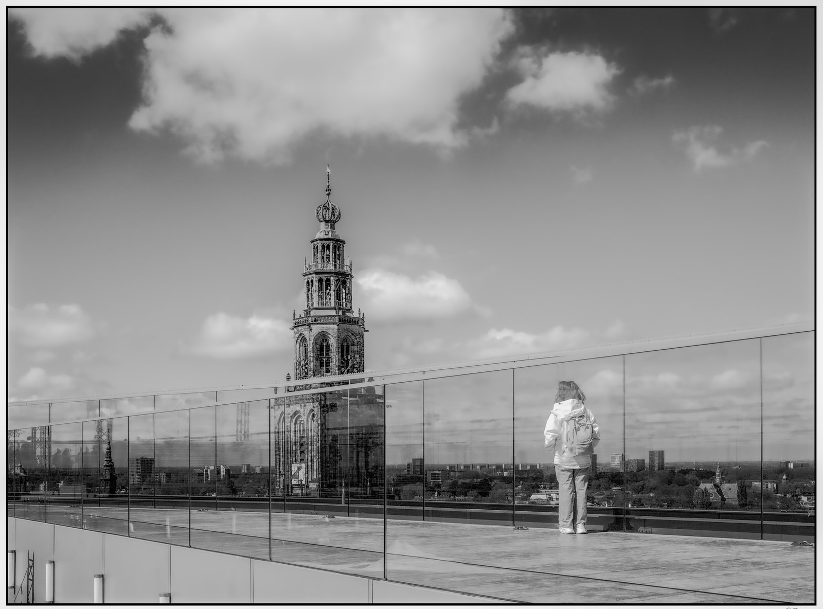 A person stands on a rooftop platform, gazing at a tall, ornate tower in the distance.