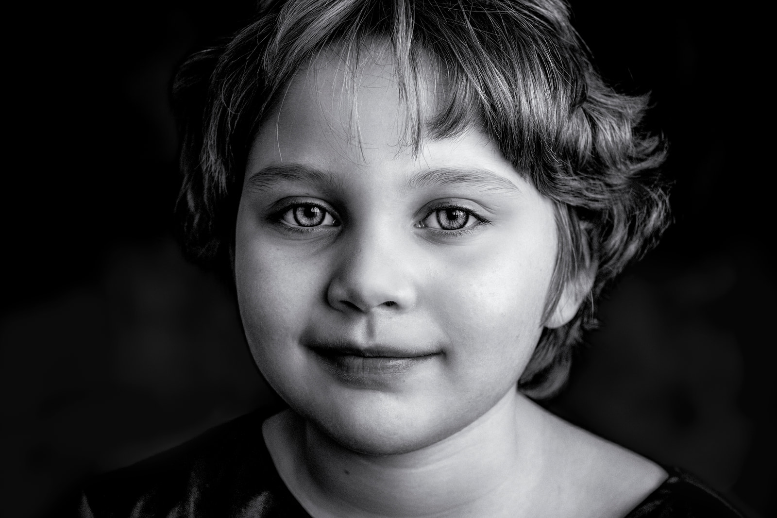 A young child smiles directly at the camera against a dark background.