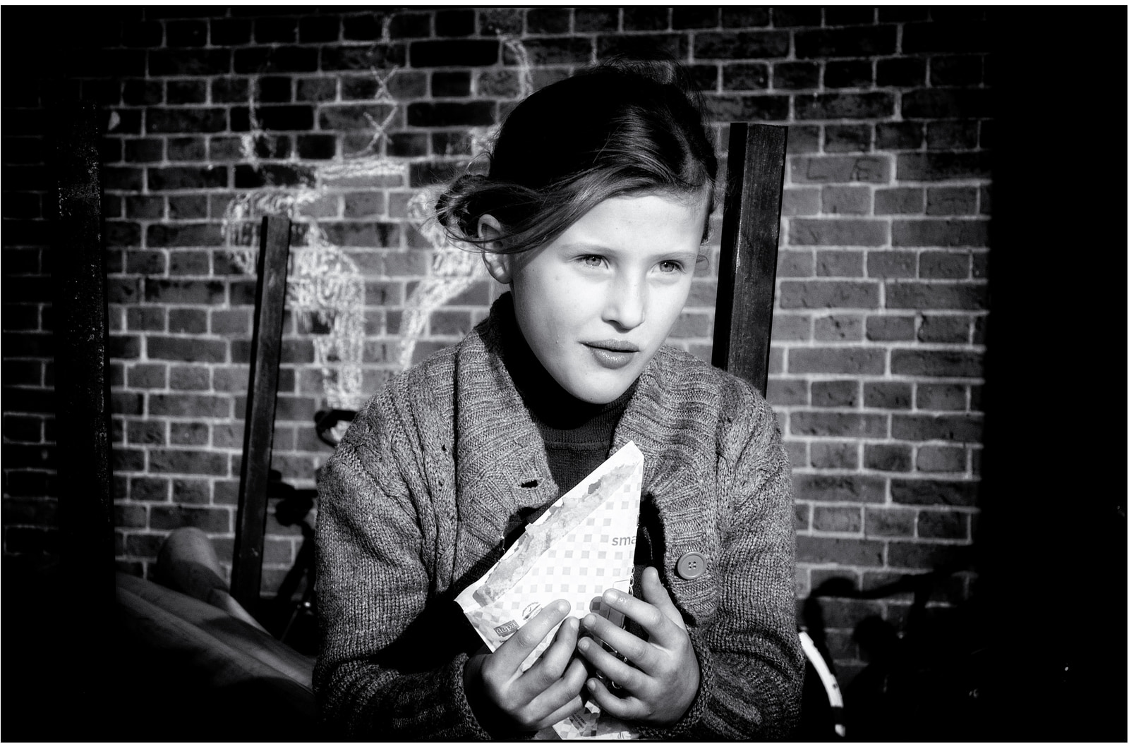 A young person sits holding a folded paper against a brick wall.