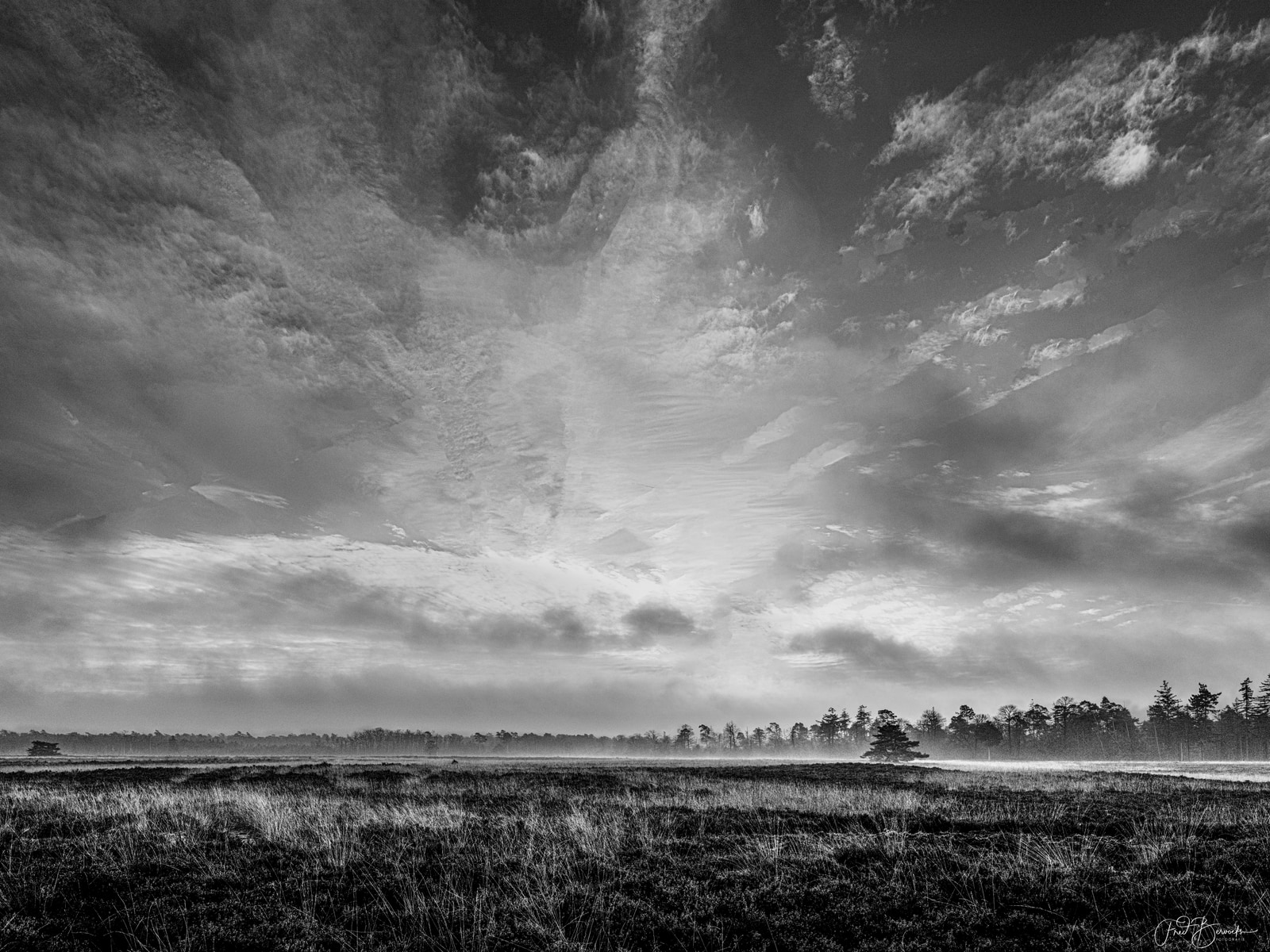 A wide, open field stretches under a dramatic, brooding sky filled with dense, dark clouds.