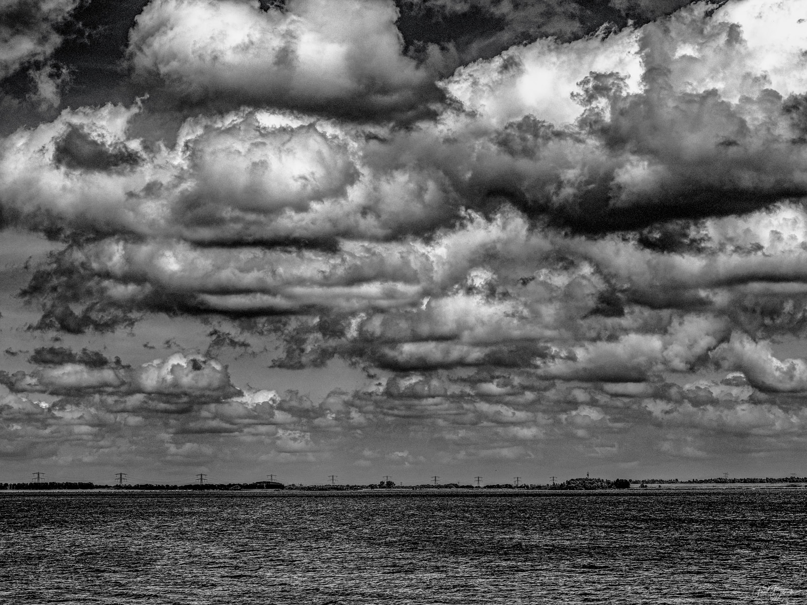 A vast expanse of turbulent clouds stretches across a dramatic sky over a calm body of water.