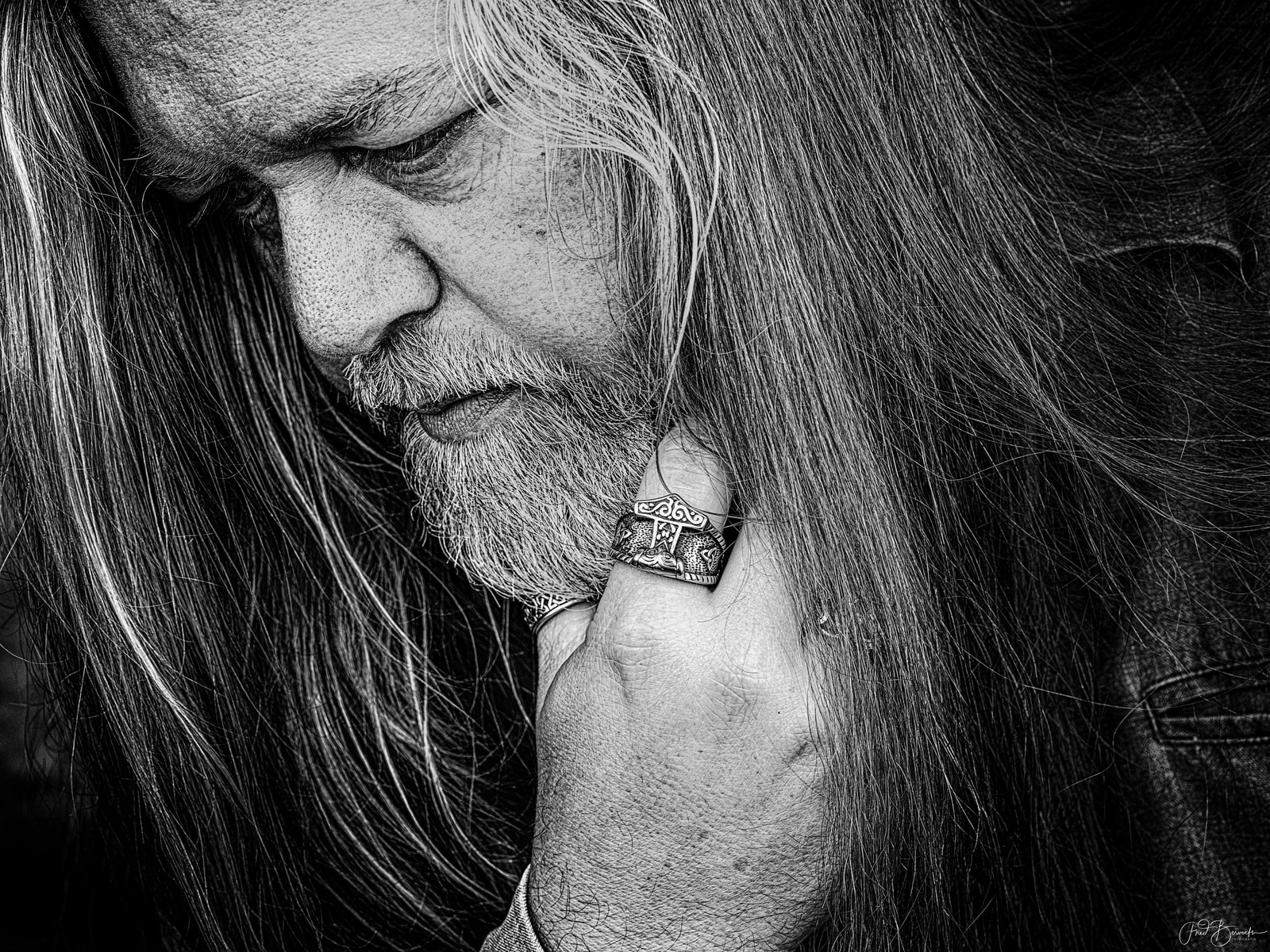 A close-up view of a bearded man with long hair, wearing a patterned bracelet on his wrist.