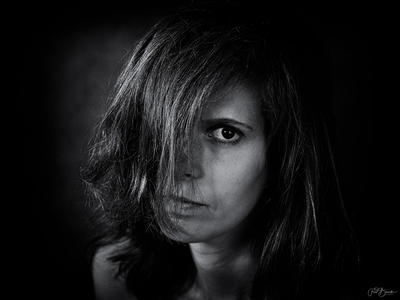 A person with long hair gazes directly at the camera against a dark background.