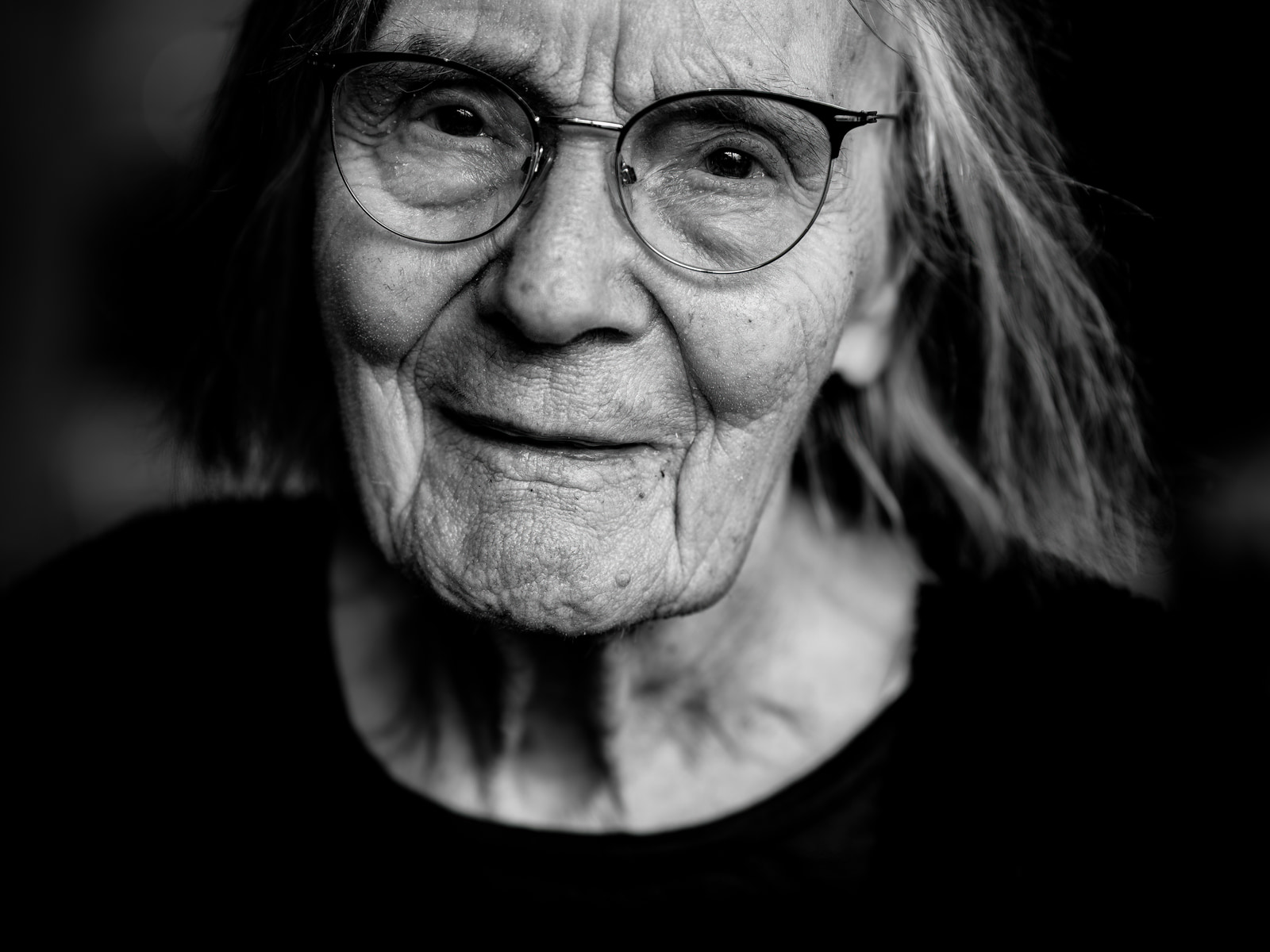 An older person with glasses looks directly at the camera.