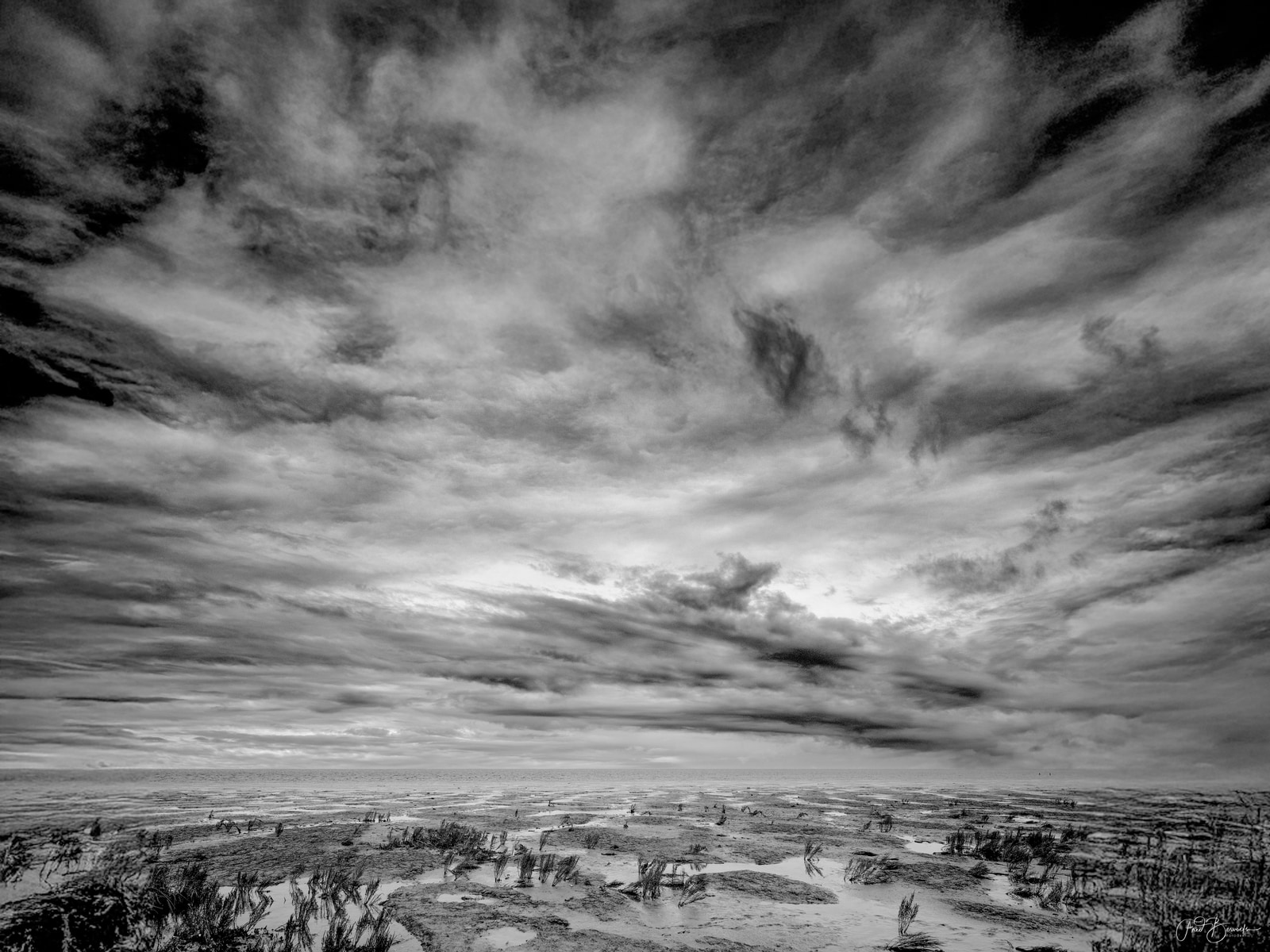 A vast, open landscape under a dramatic, brooding sky with dense, layered clouds.