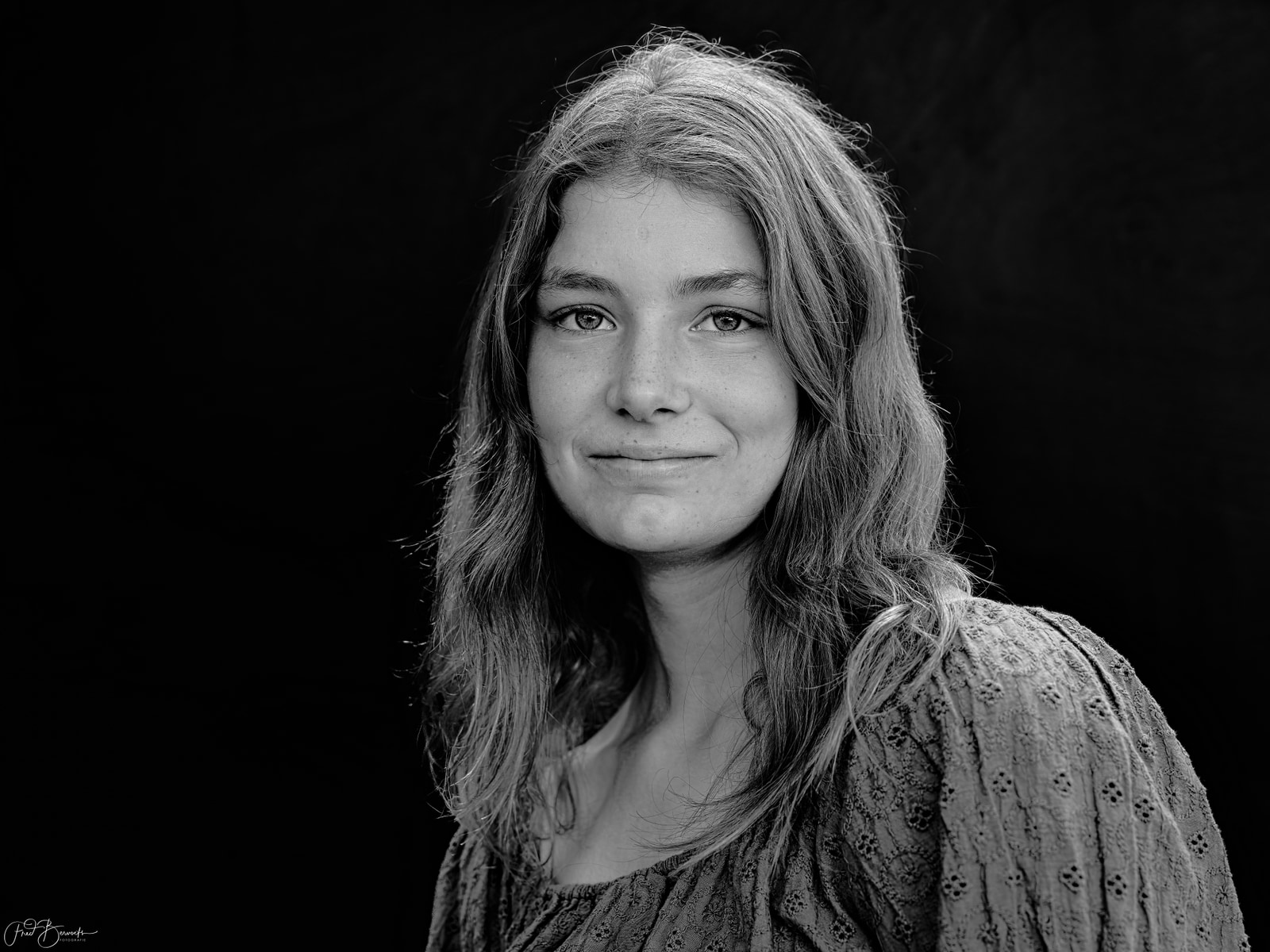 A person with long hair is shown in a close-up portrait against a dark background.