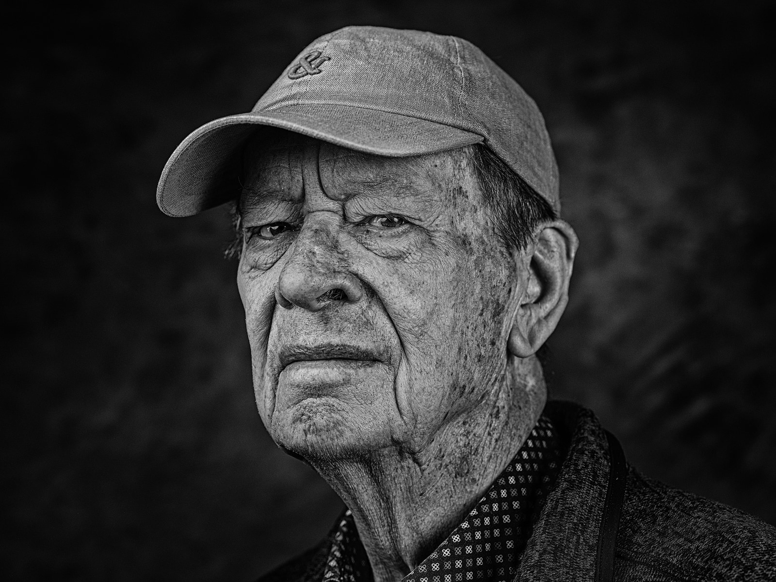 An older man with a cap looks directly at the camera.
