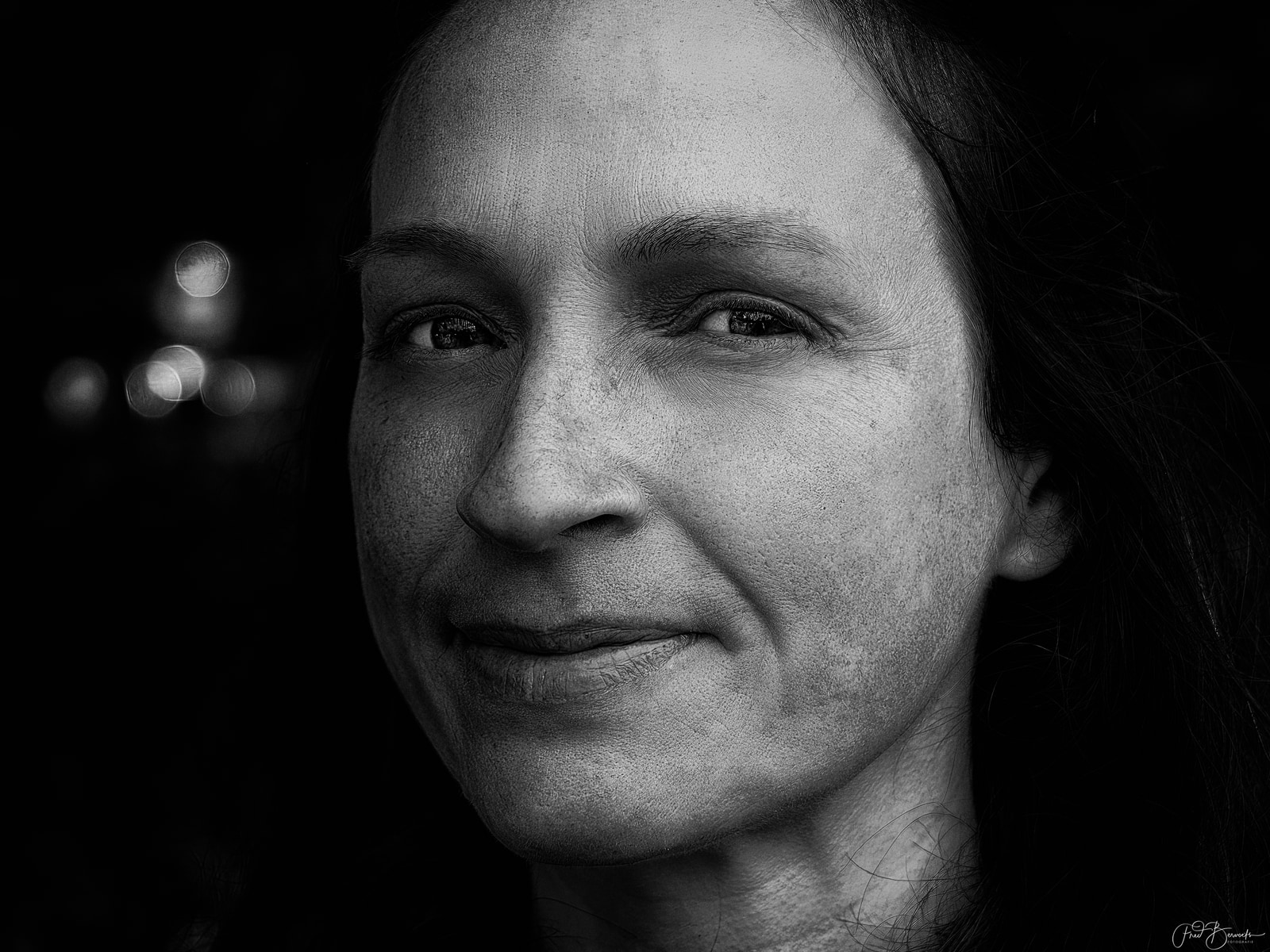 A close-up portrait of an individual with long hair, captured in black and white with soft, diffused lighting.