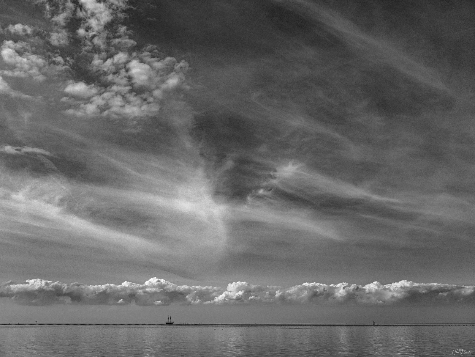 A vast, brooding sky with dramatic clouds stretches over a calm sea, with a distant ship barely visible on the horizon.