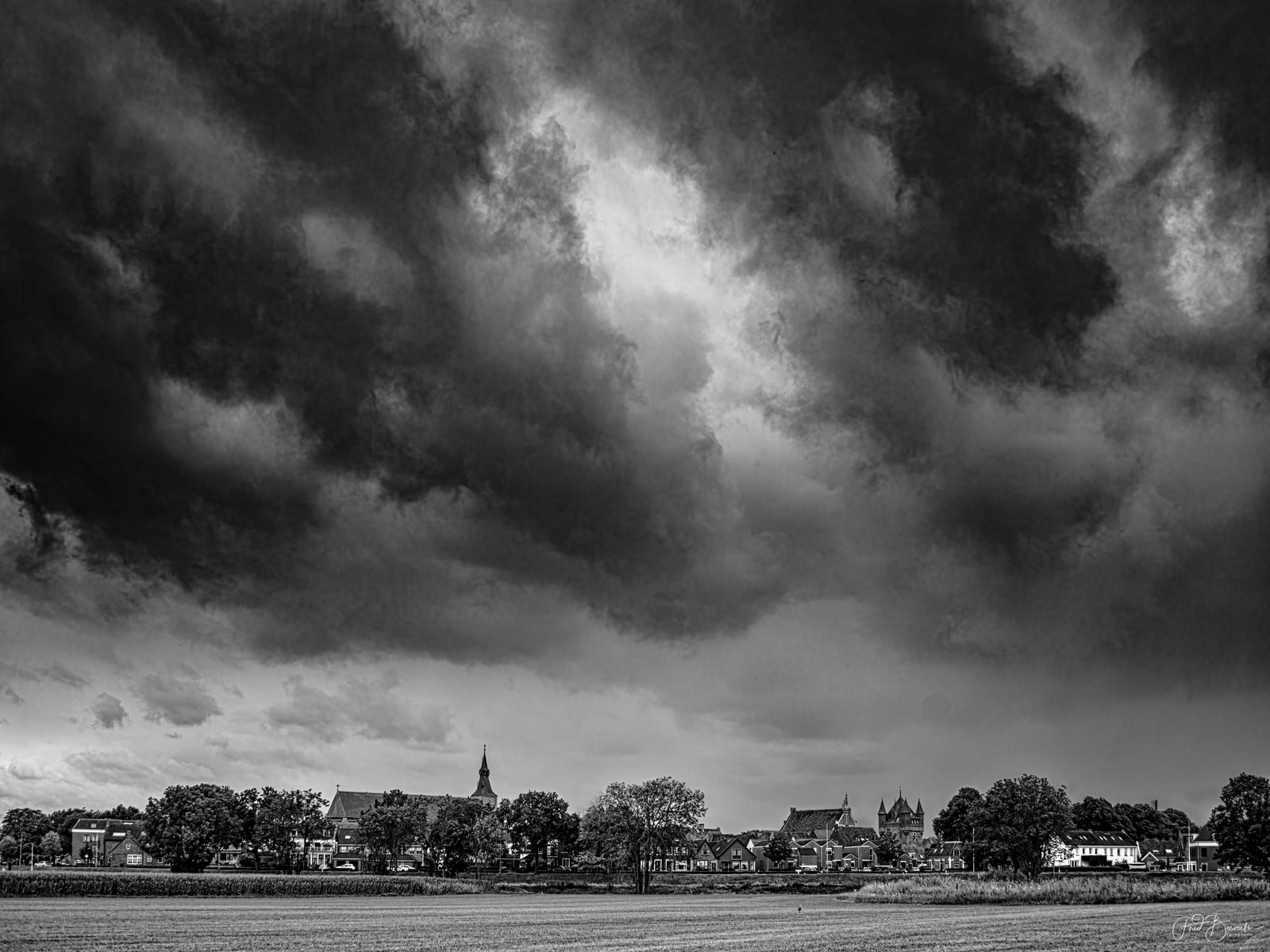 A dramatic sky with dark, heavy clouds looms over a small village with visible houses and a church tower.