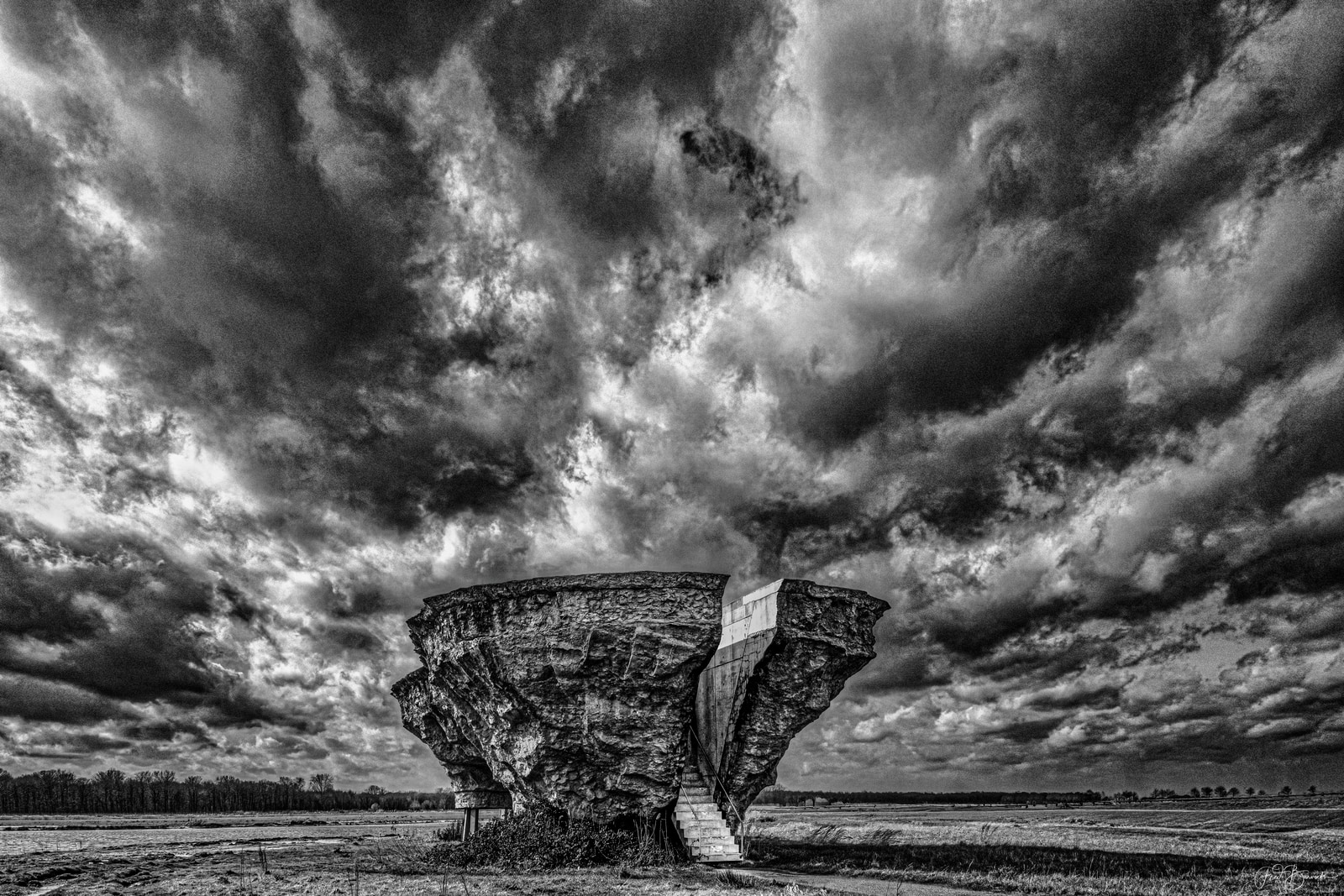 A large, weathered concrete structure stands prominently against a dramatic, brooding sky filled with dense, dark clouds.