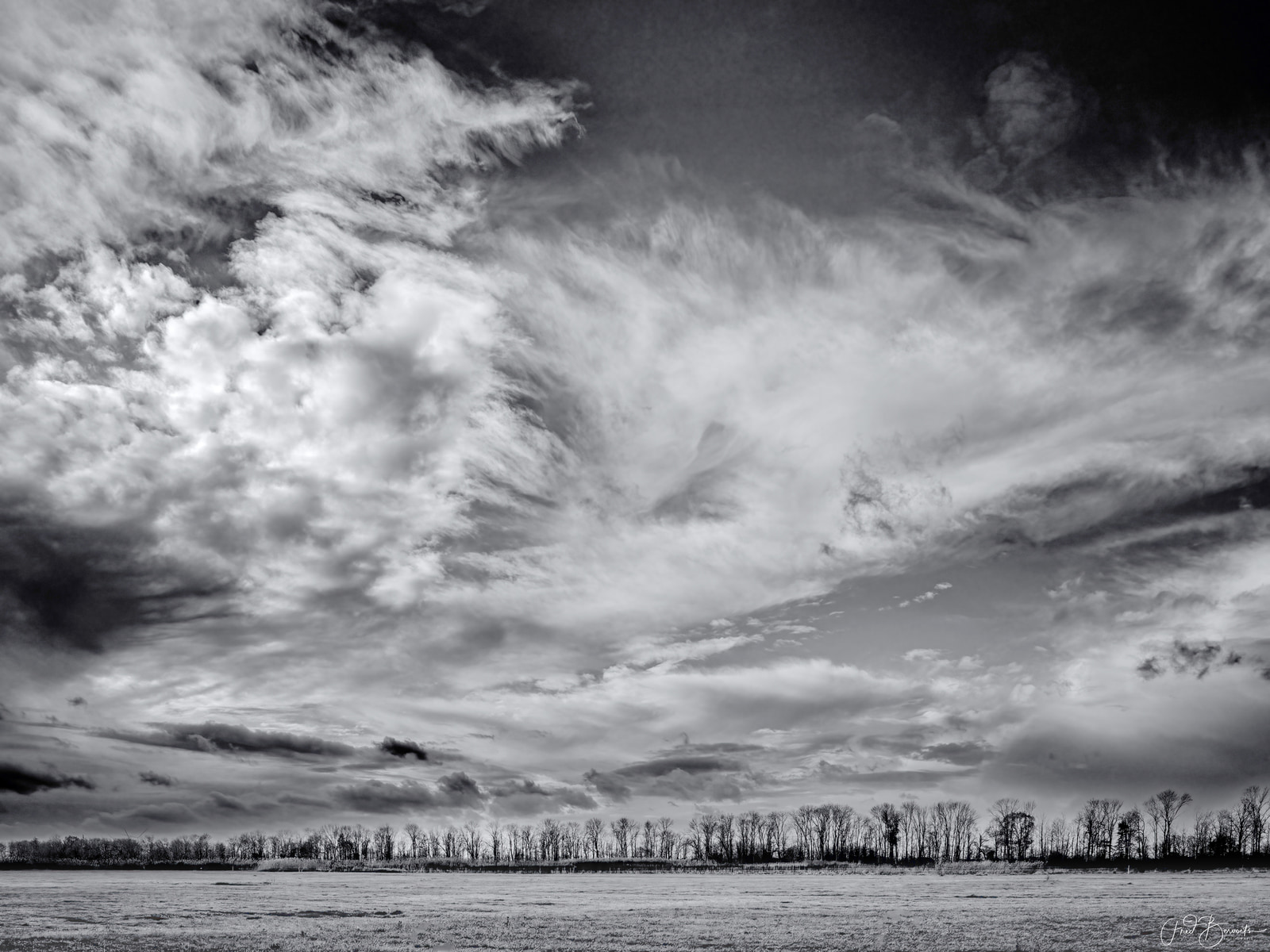 A vast field stretches beneath a dramatic sky filled with dense, billowing clouds.