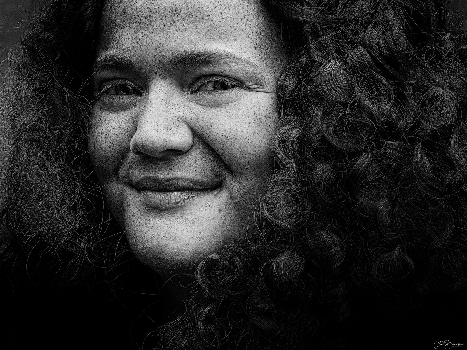 A close-up portrait of a person with curly hair, smiling gently.
