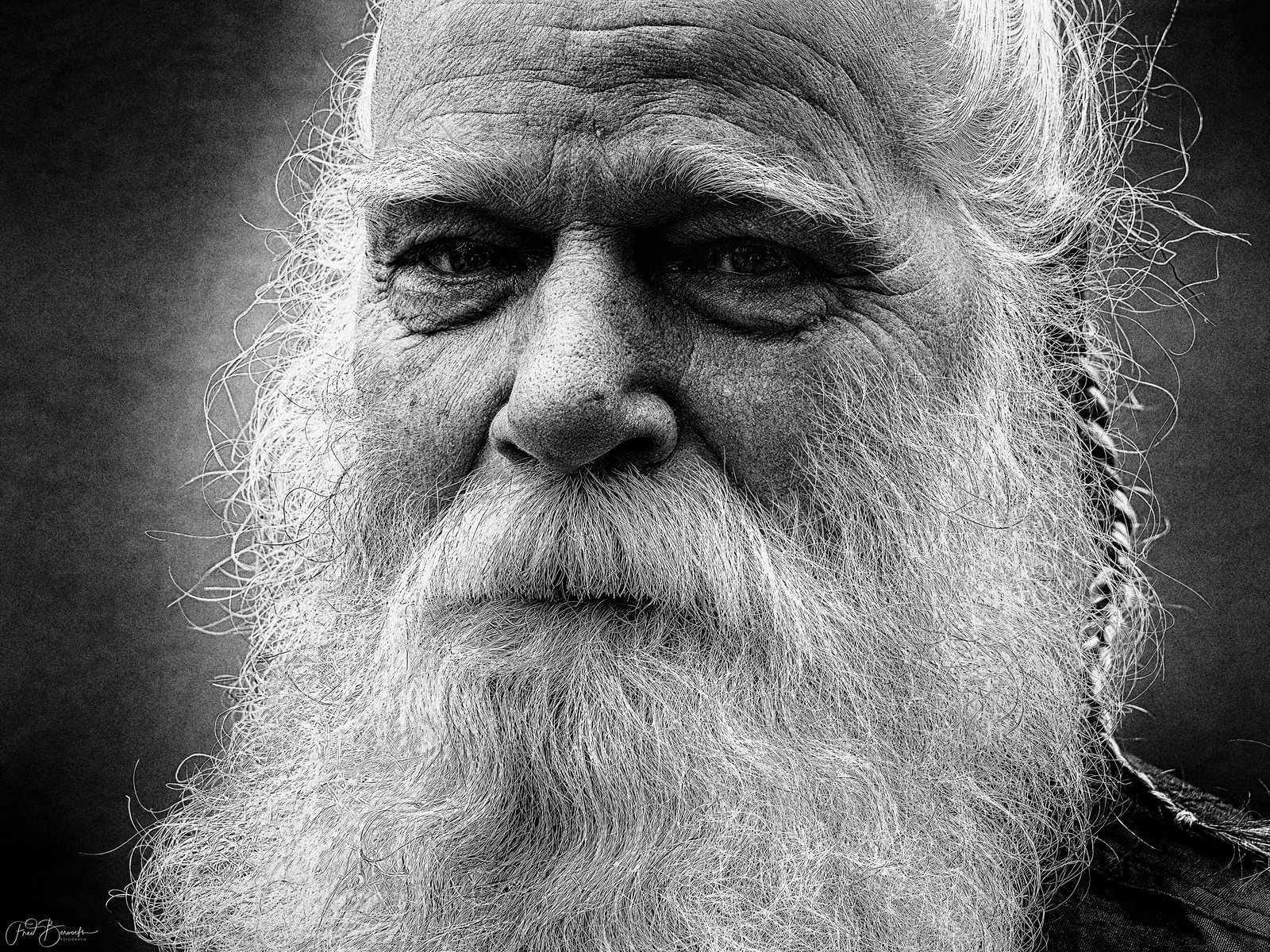 A close-up portrait of an elderly man with a long white beard and hair, his eyes closed, captured in black and white.