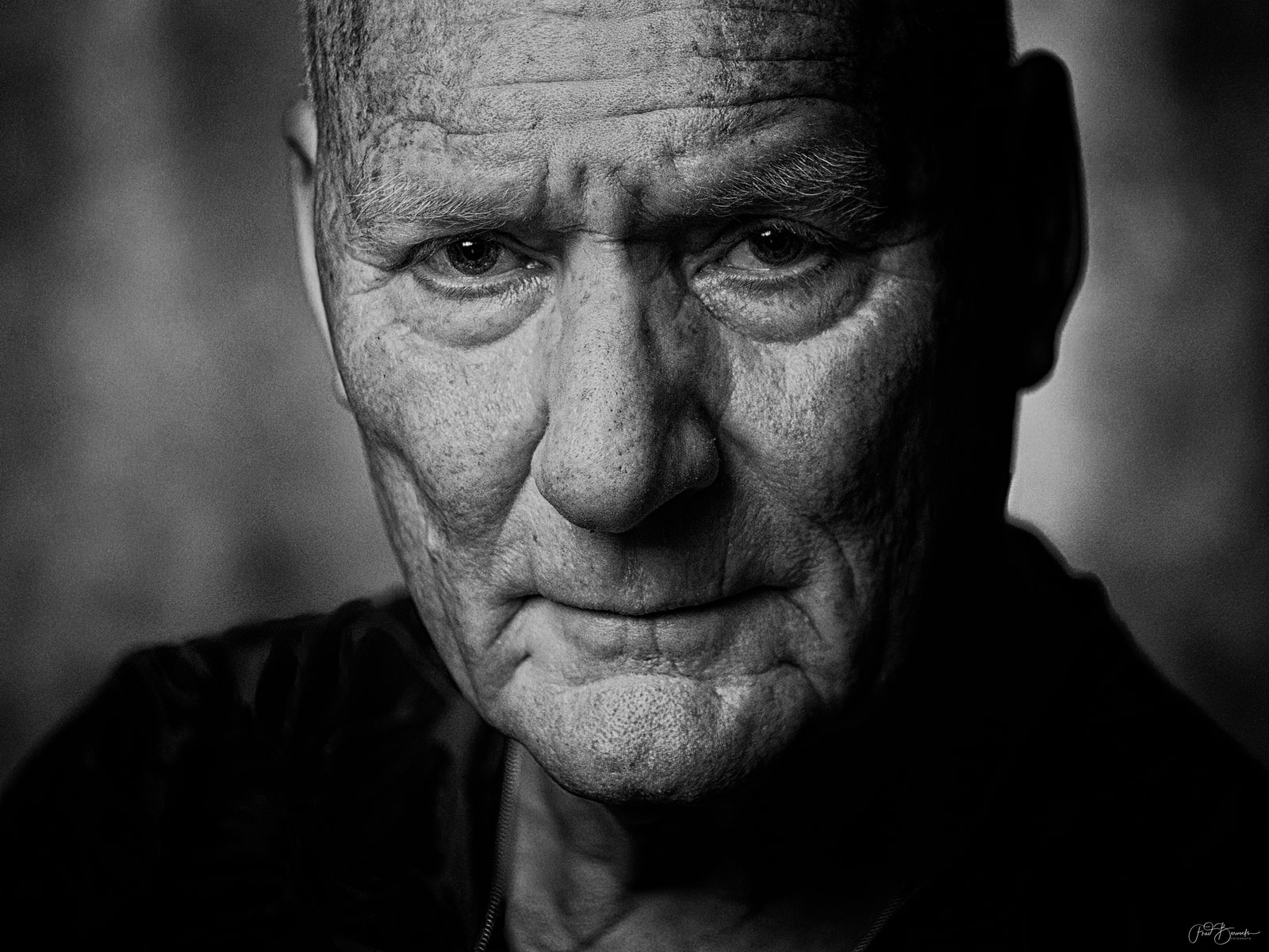 An older man with a serious expression is shown in a close-up portrait.
