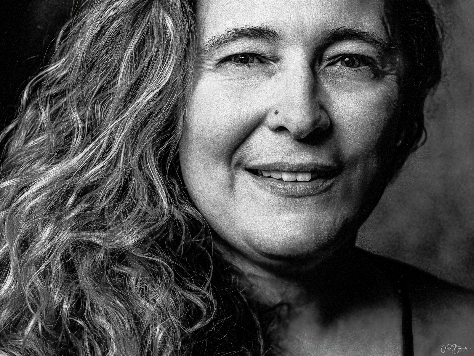 A close-up portrait of a person with long hair, smiling gently against a dark background.